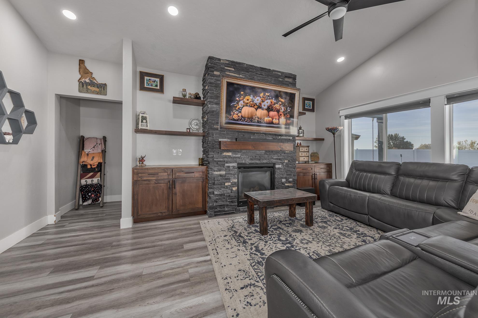 Living room featuring recessed lighting, light wood-type flooring, a stone fireplace, ceiling fan, and lofted ceiling