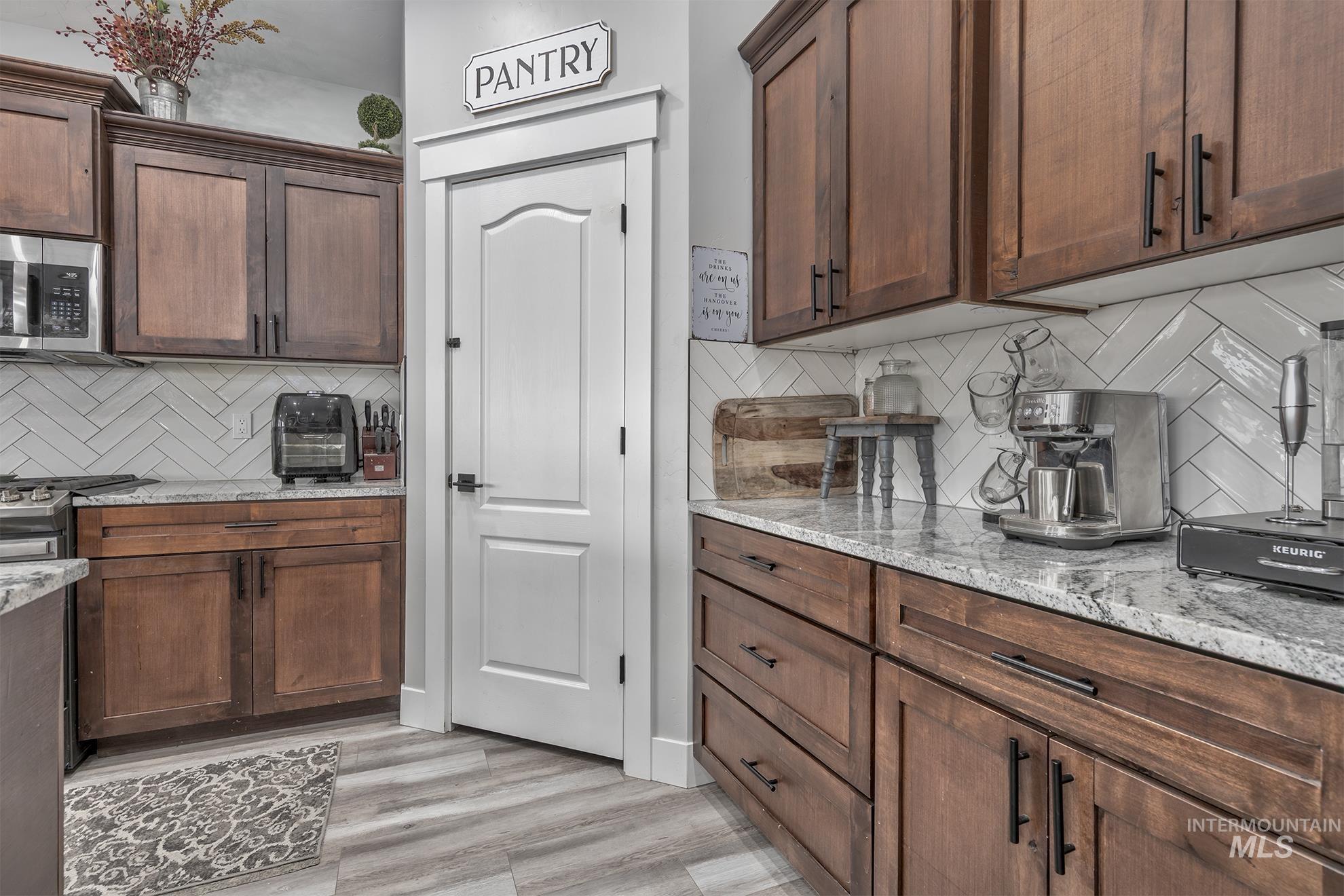 Kitchen with backsplash, light stone counters, stainless steel appliances, and light wood-type flooring