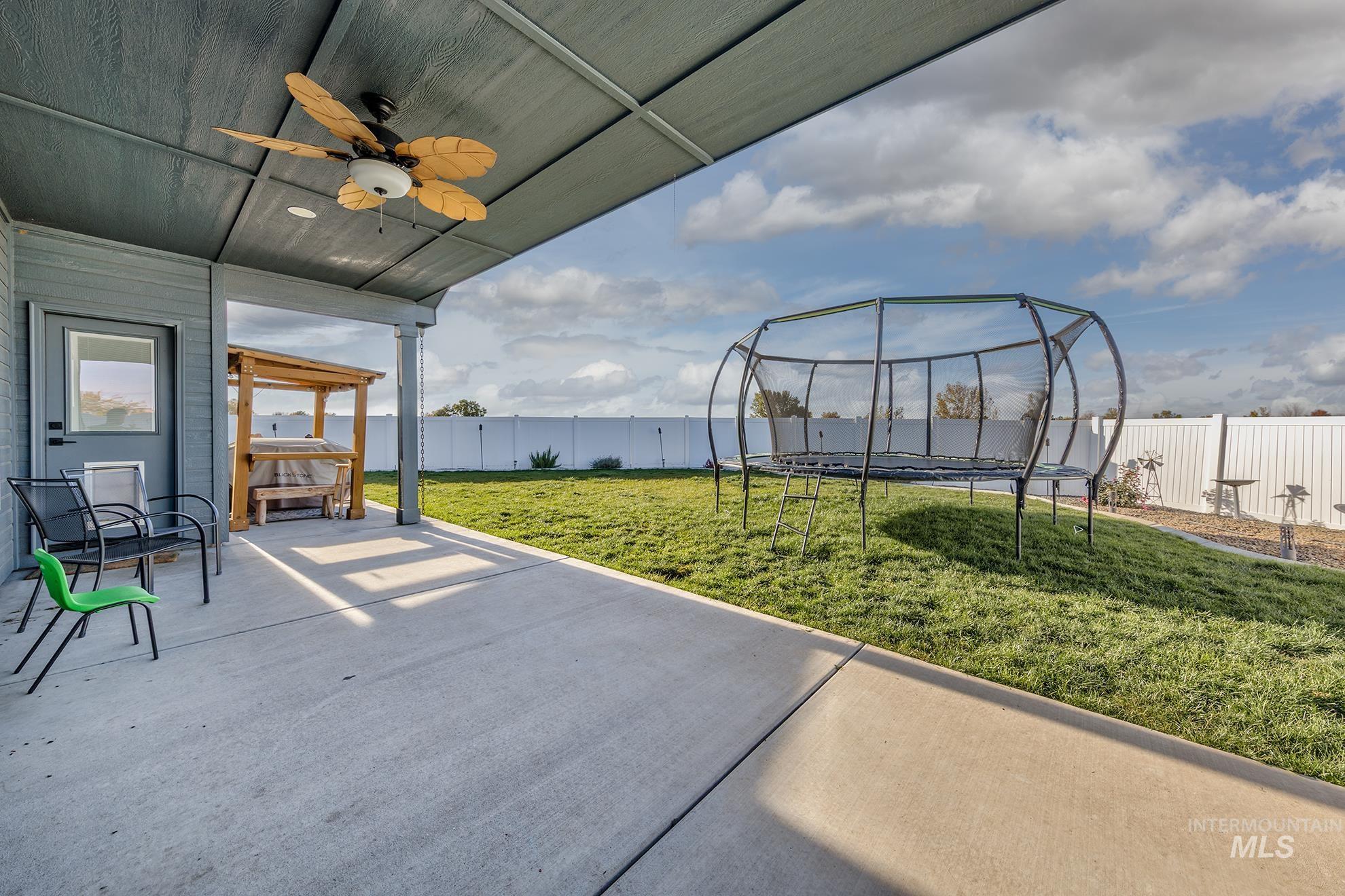 Fenced backyard featuring a trampoline, a ceiling fan, and a patio area