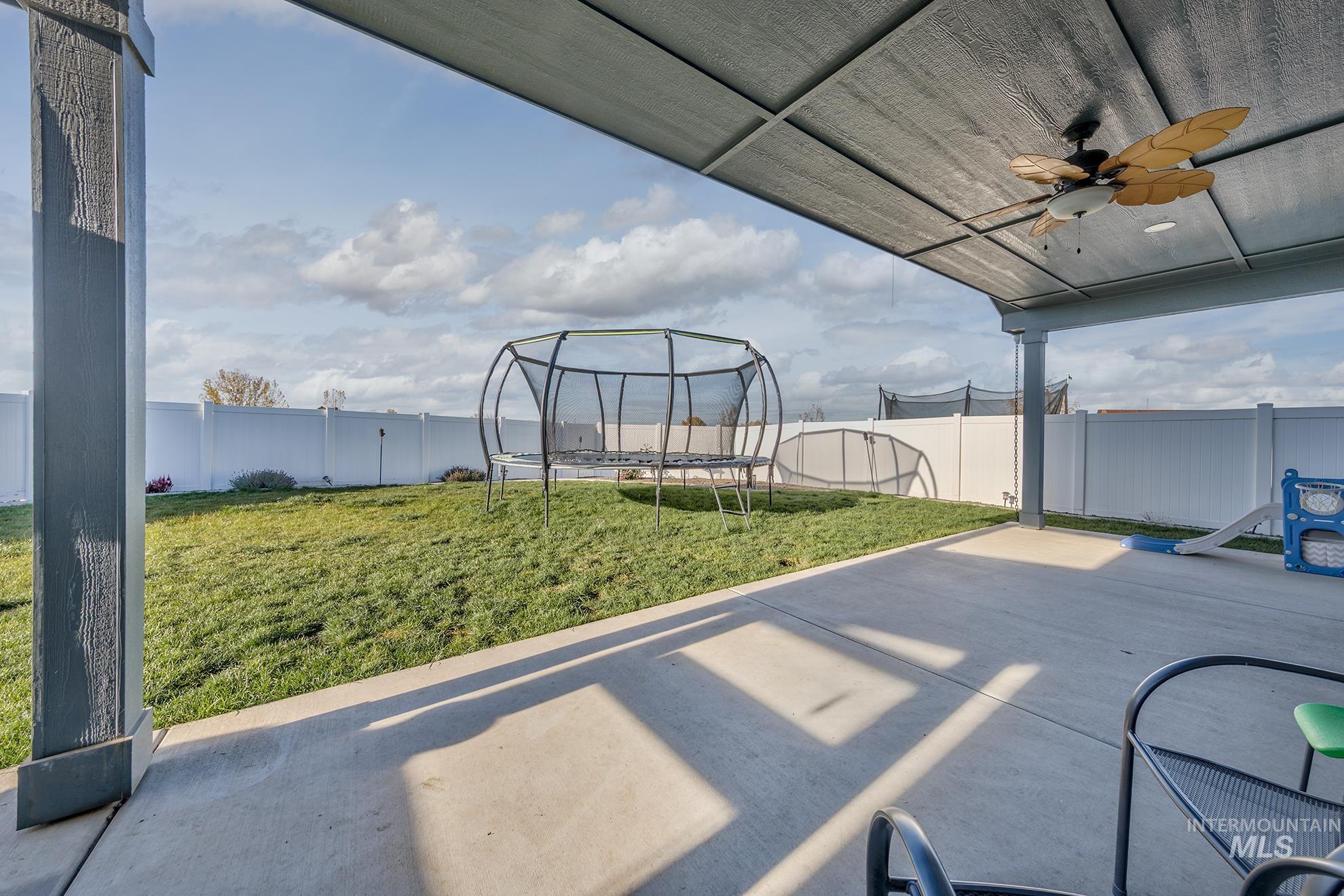 Fenced backyard with a trampoline, a patio area, and ceiling fan