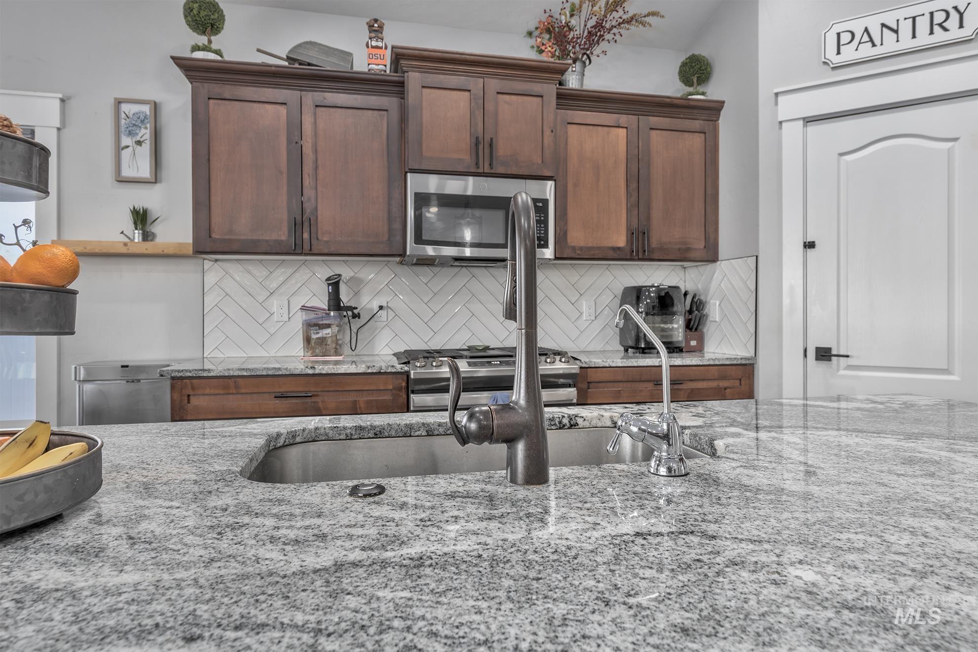 Kitchen with backsplash, appliances with stainless steel finishes, light stone countertops, and dark brown cabinetry