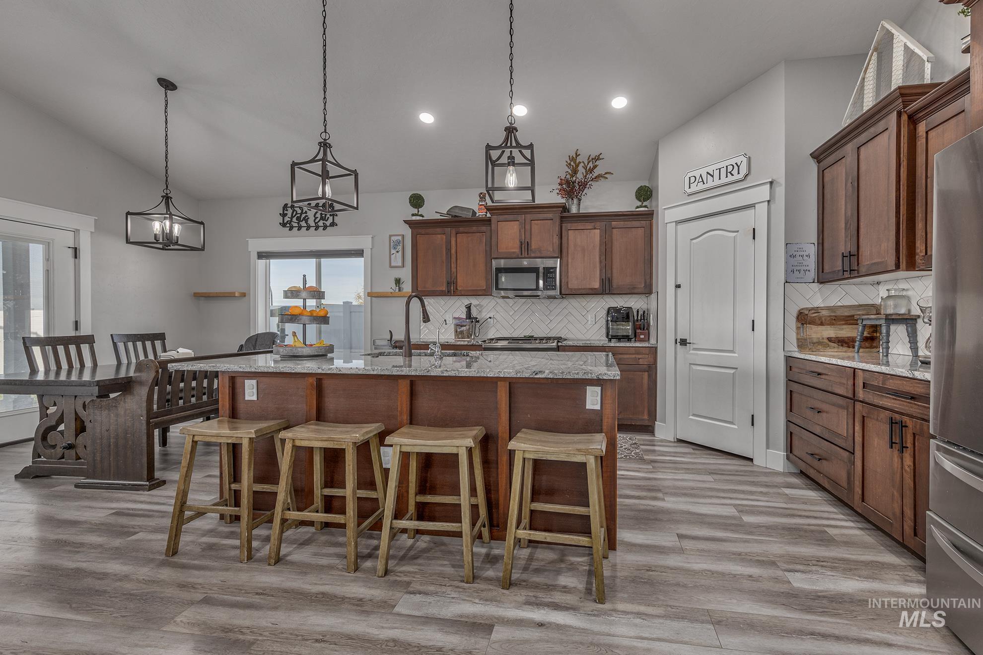 Kitchen with decorative light fixtures, light stone countertops, lofted ceiling, a breakfast bar, and a kitchen island with sink