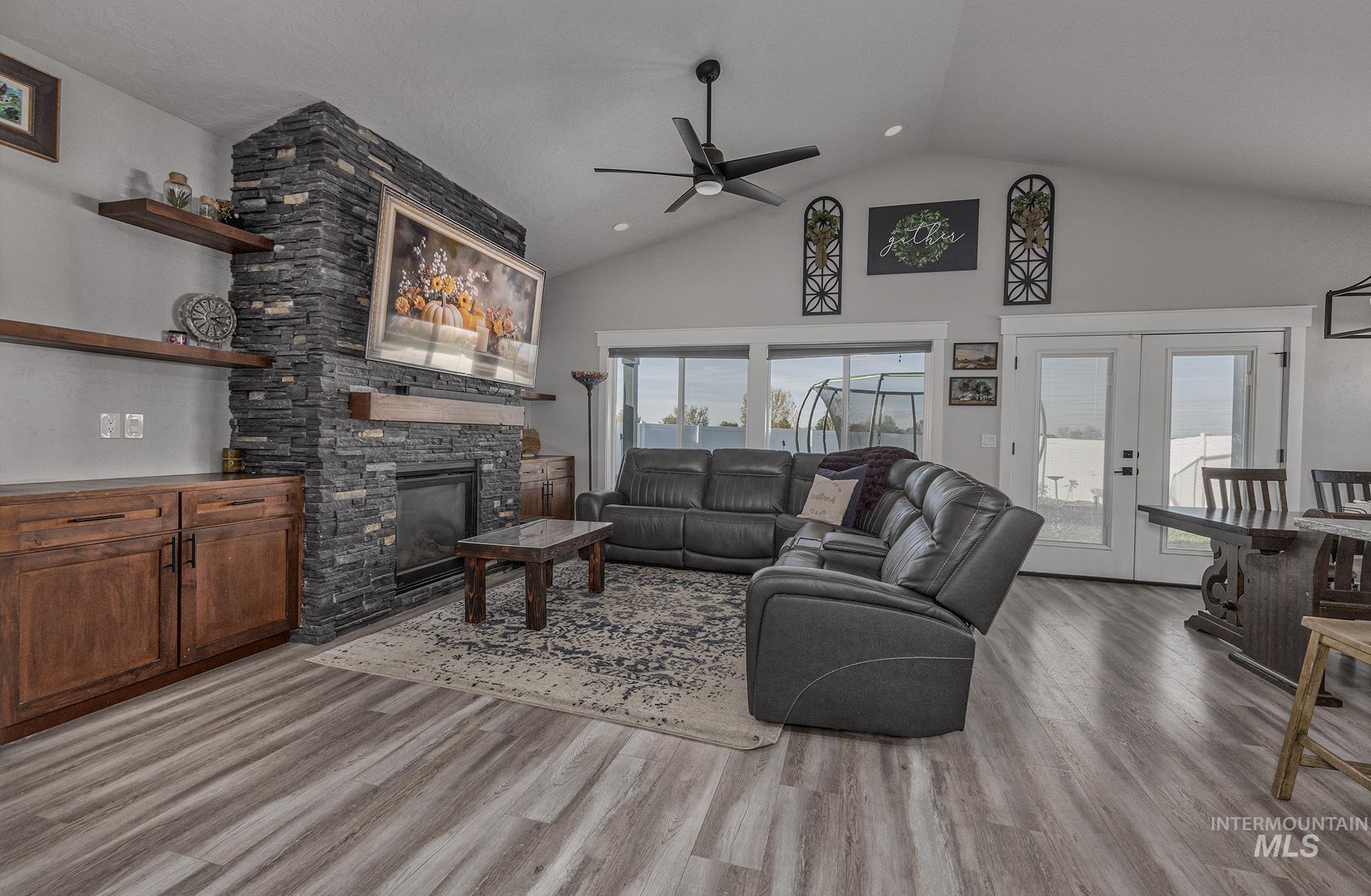 Living area featuring high vaulted ceiling, french doors, light wood-type flooring, a stone fireplace, and a ceiling fan