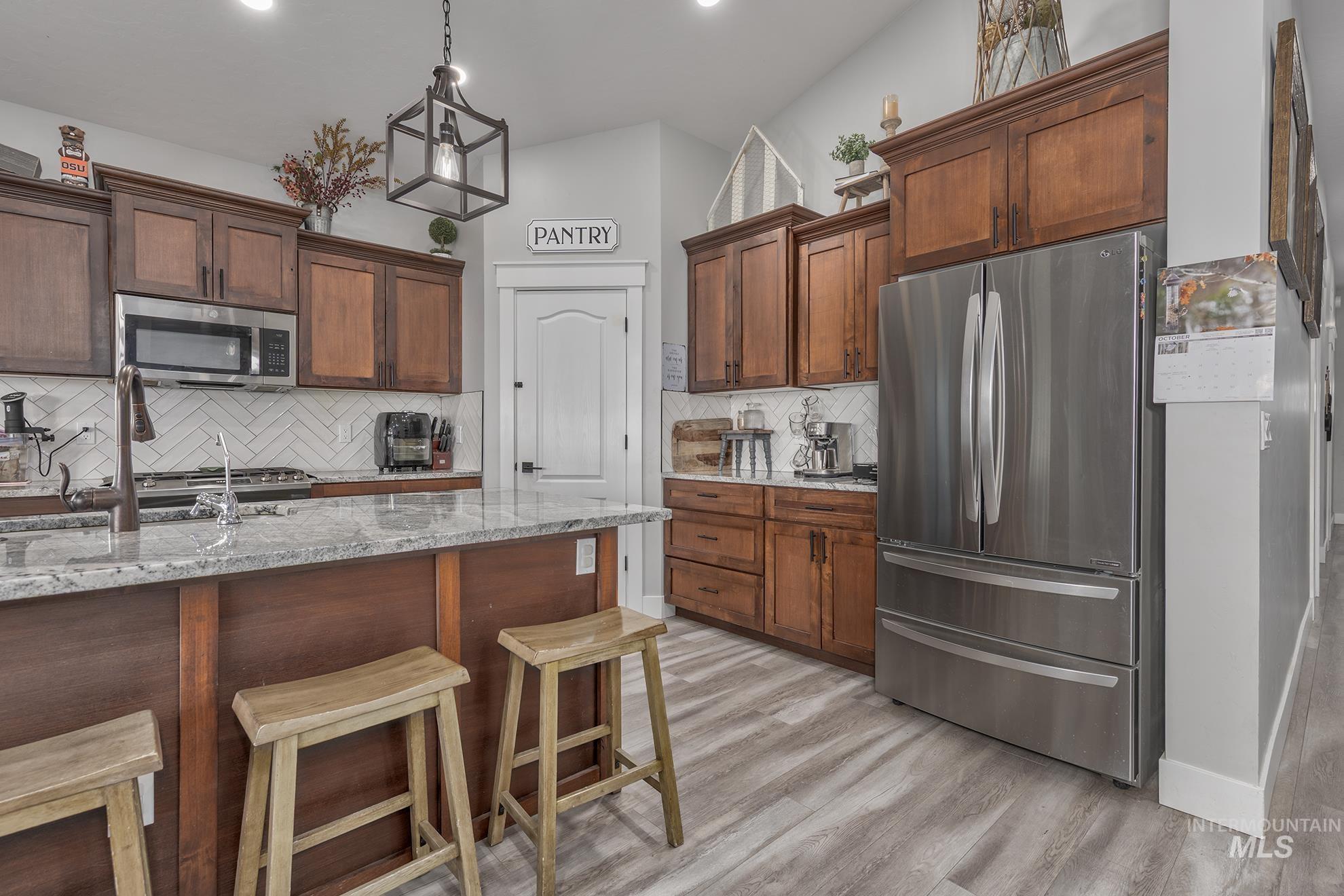 Kitchen with light stone countertops, stainless steel appliances, pendant lighting, tasteful backsplash, and light wood-style floors