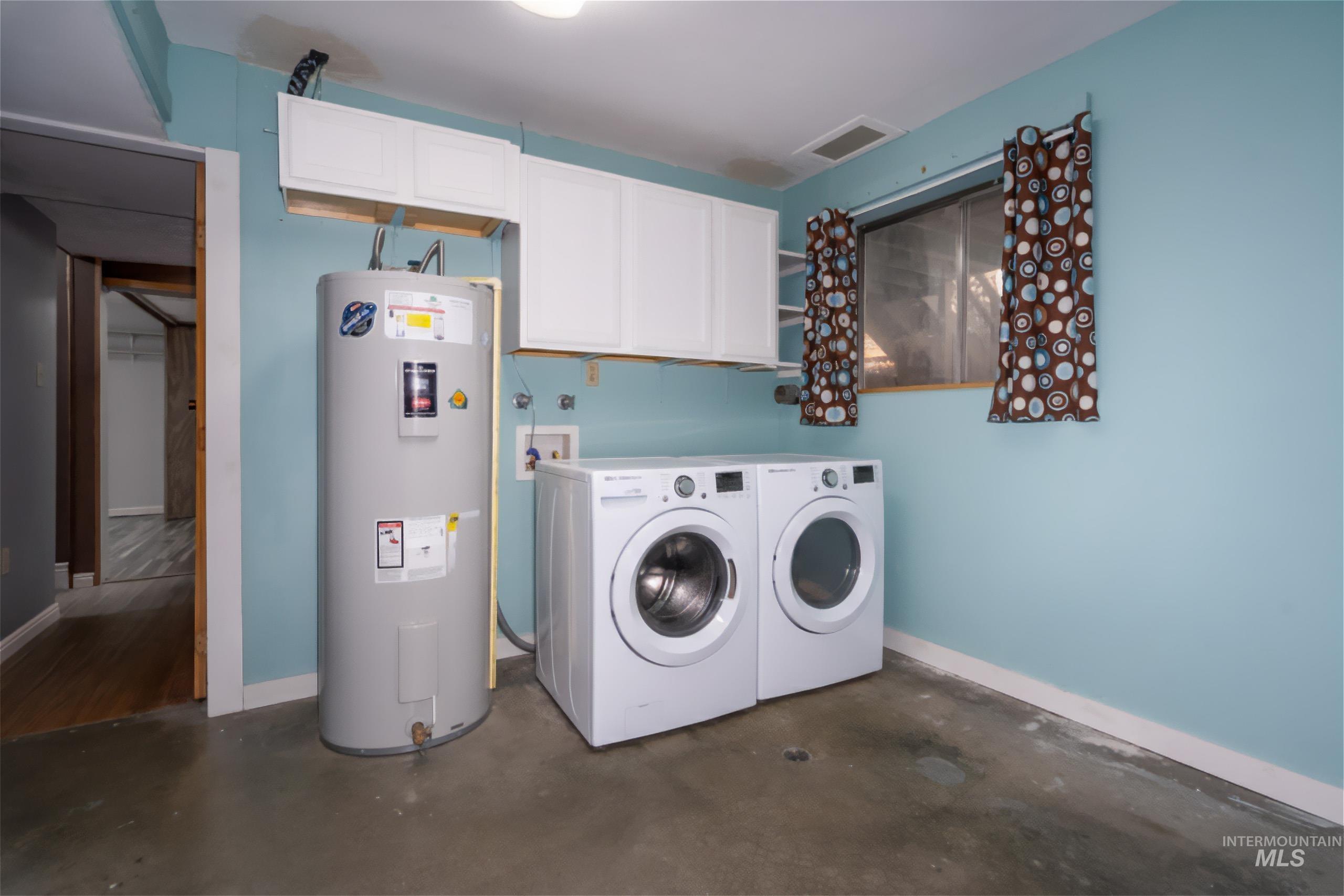 Washroom with electric water heater, concrete floors, cabinet space, and separate washer and dryer