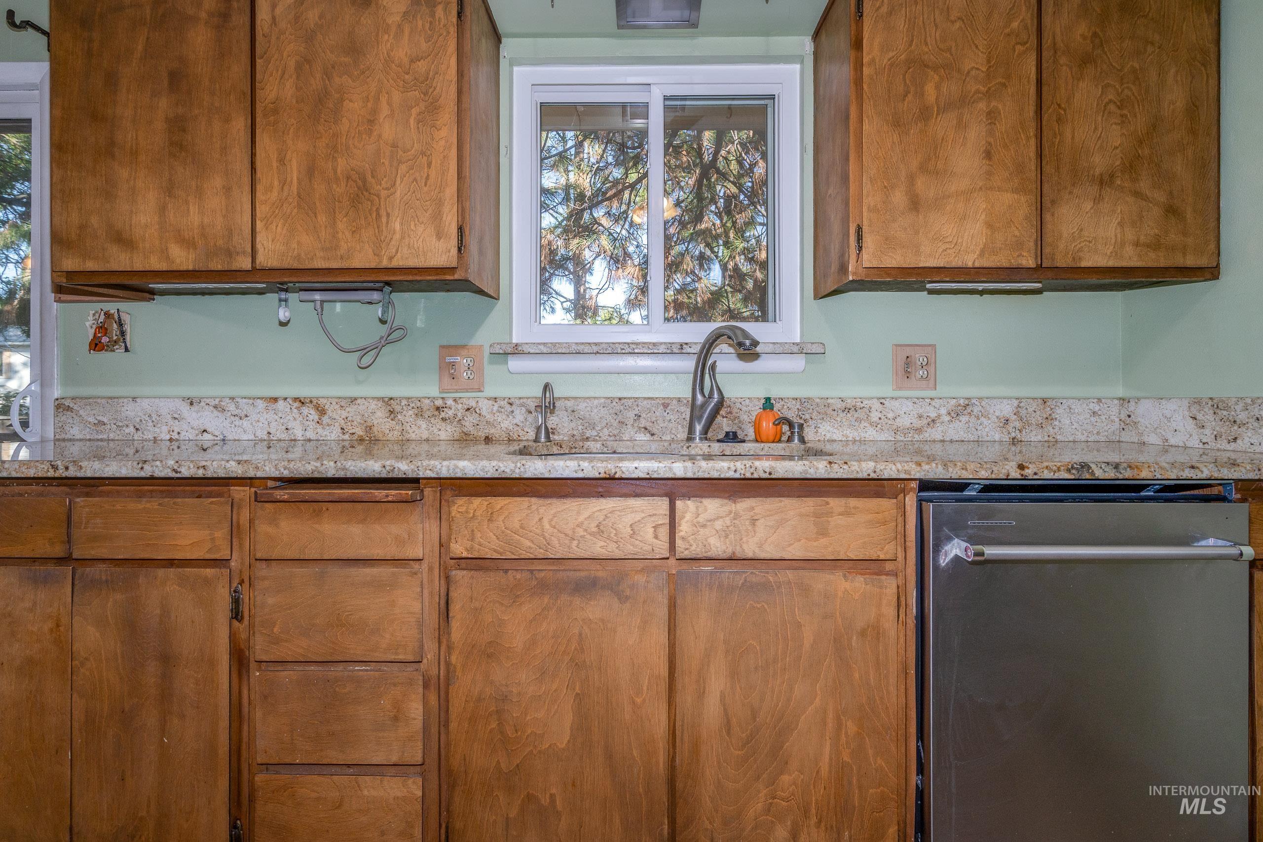 Kitchen featuring dishwasher, brown cabinetry, plenty of natural light, and light stone countertops