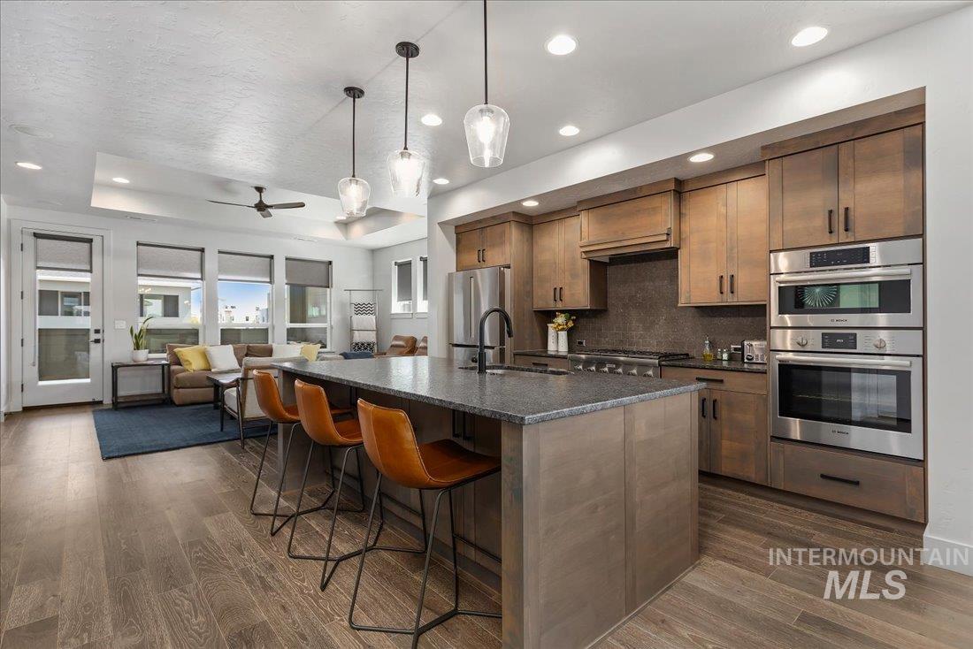 Kitchen featuring ceiling fan, decorative light fixtures, a kitchen breakfast bar, stainless steel appliances, and a kitchen island with sink