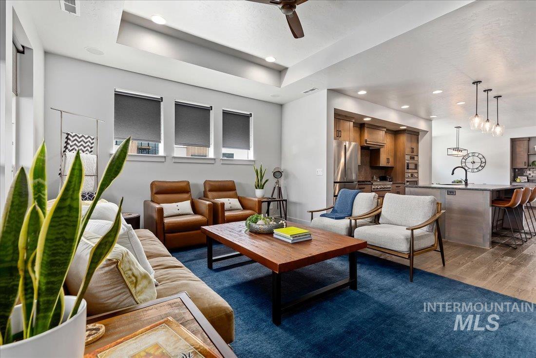 Living room featuring light wood finished floors, ceiling fan, a tray ceiling, and recessed lighting