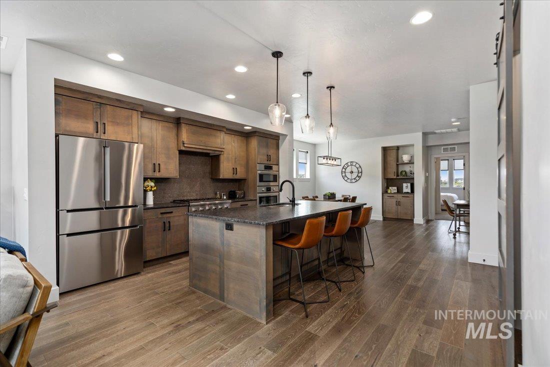 Kitchen with stainless steel appliances, a breakfast bar, a kitchen island with sink, hanging light fixtures, and dark wood finished floors