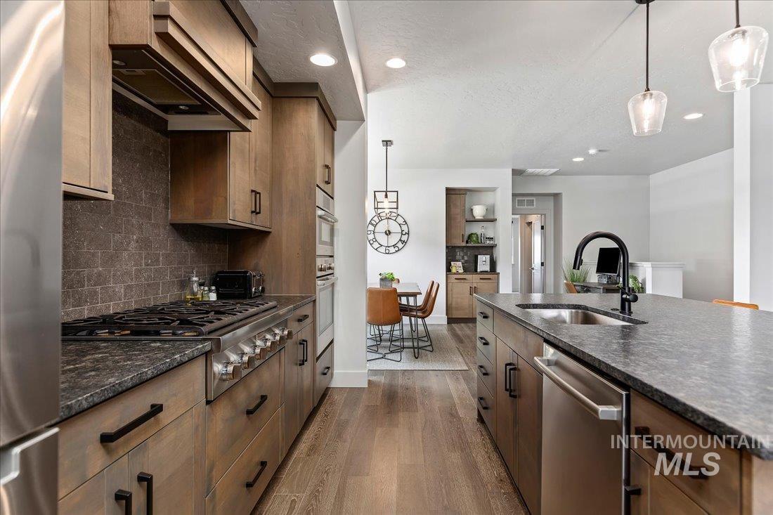Kitchen with hanging light fixtures, custom exhaust hood, a textured ceiling, stainless steel appliances, and dark stone counters