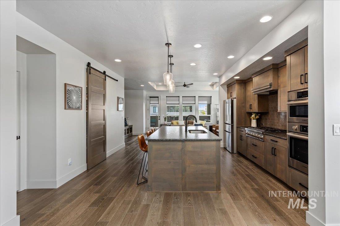 Kitchen with a kitchen island with sink, a barn door, a kitchen bar, dark wood-style floors, and decorative backsplash