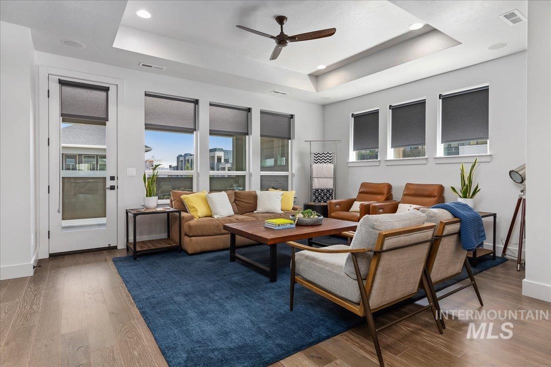 Living room with healthy amount of natural light, a raised ceiling, wood finished floors, ceiling fan, and recessed lighting