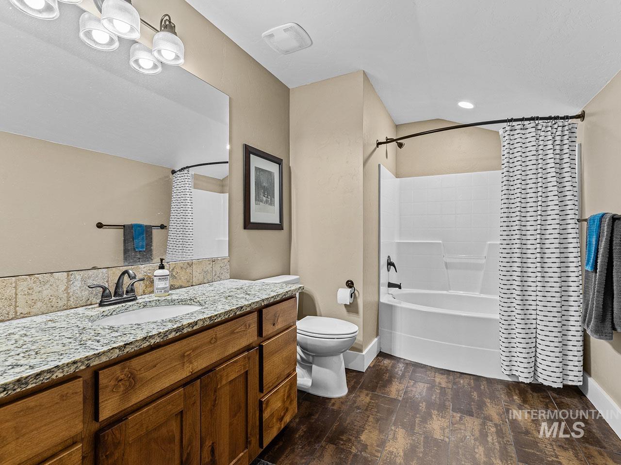 Bathroom with wood finished floors, vanity, and shower / bath combination with curtain