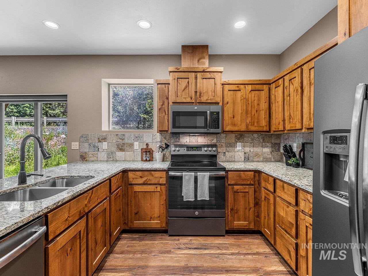 Kitchen featuring stainless steel appliances, backsplash, light stone counters, wood finished floors, and recessed lighting
