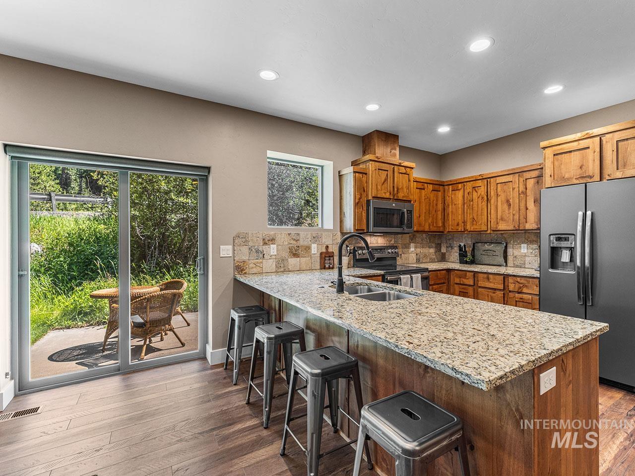 Kitchen with appliances with stainless steel finishes, recessed lighting, a peninsula, wood finished floors, and brown cabinets