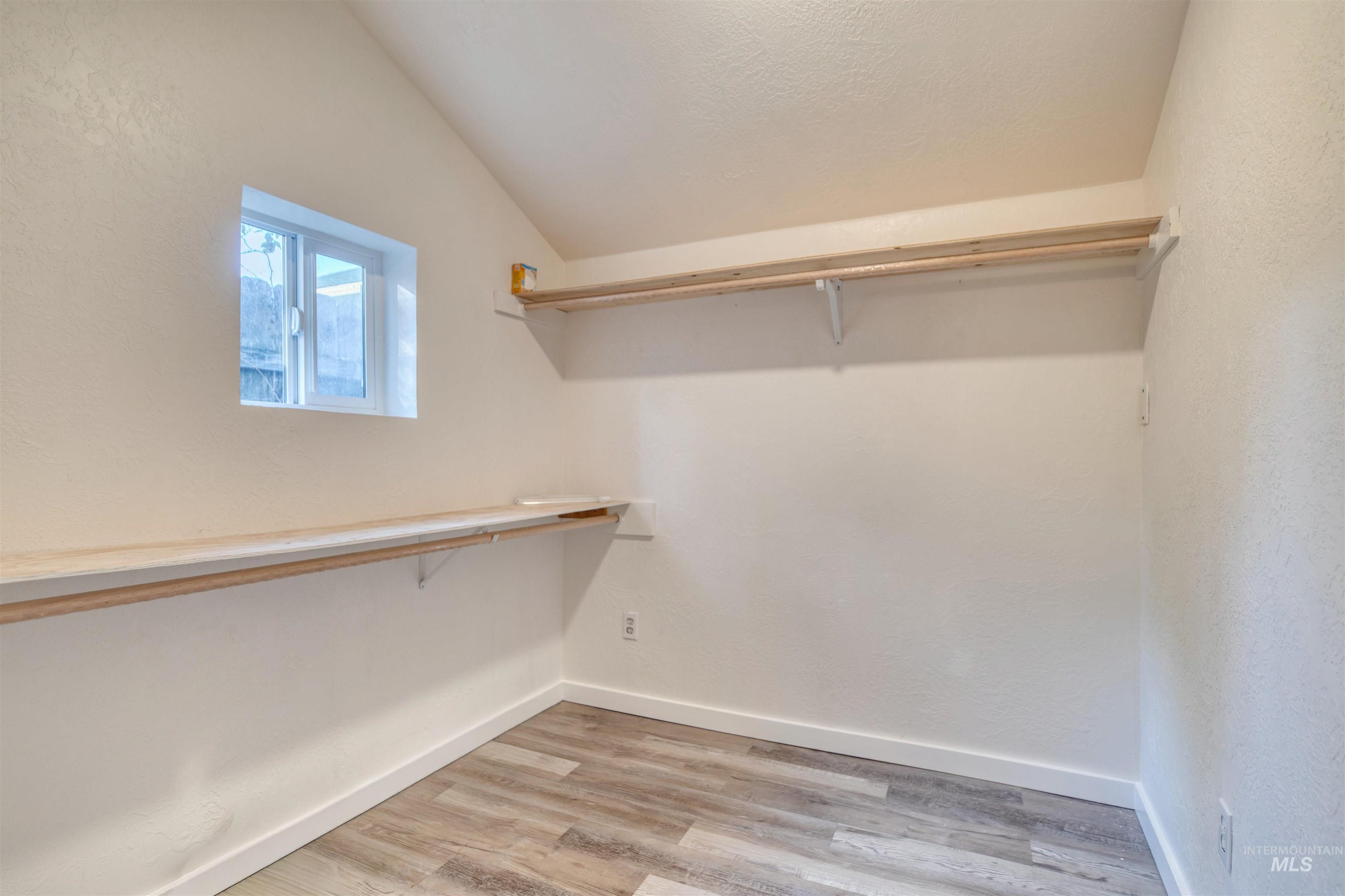 Walk in closet with light wood finished floors and lofted ceiling