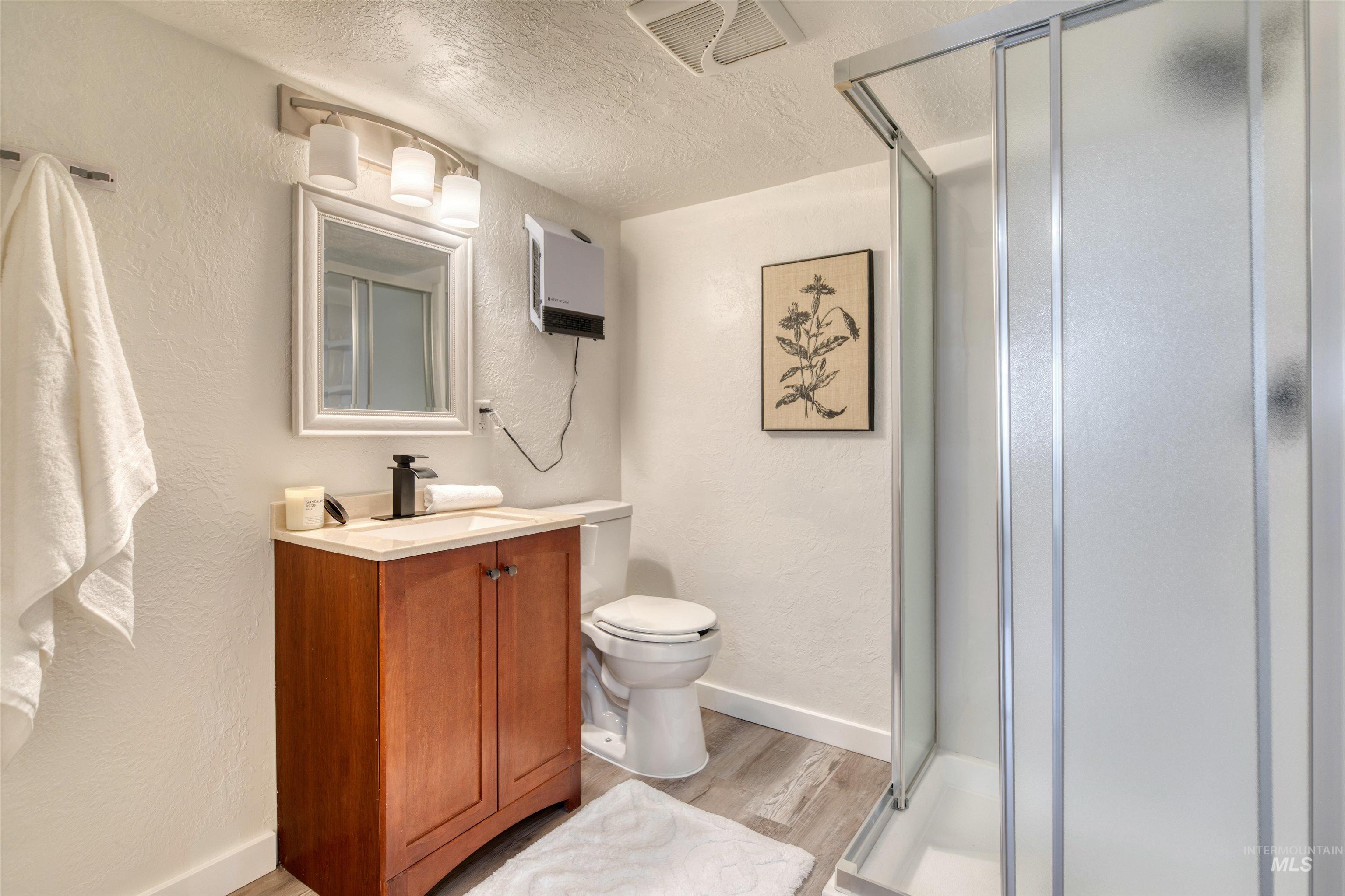 Bathroom with a textured wall, a textured ceiling, a shower stall, light wood-style floors, and vanity