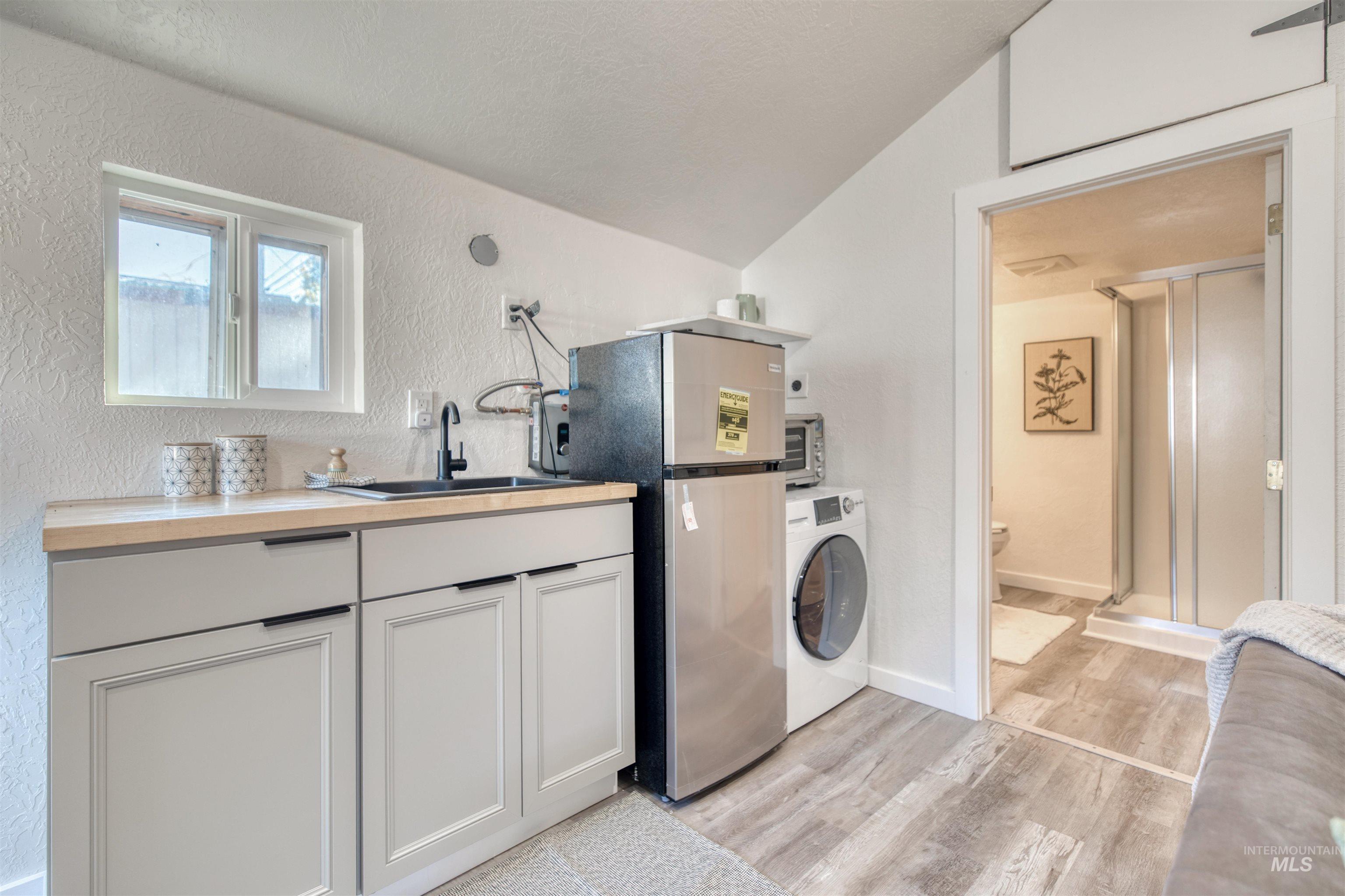 Laundry room featuring washer / dryer, a textured wall, light wood-style floors, and vaulted ceiling