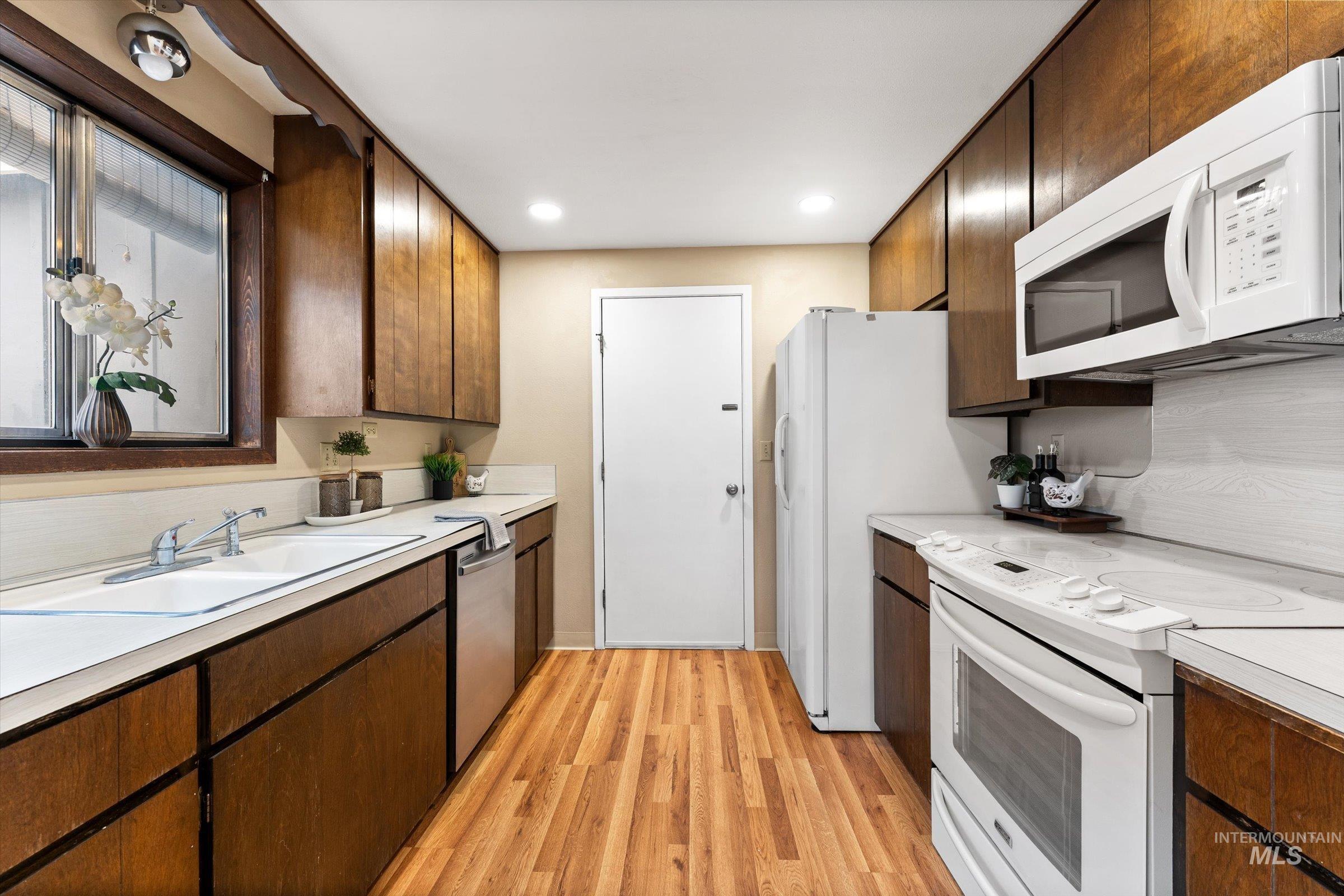 Kitchen featuring white appliances, light countertops, light wood-style flooring, recessed lighting, and dark wood finish cabinetry