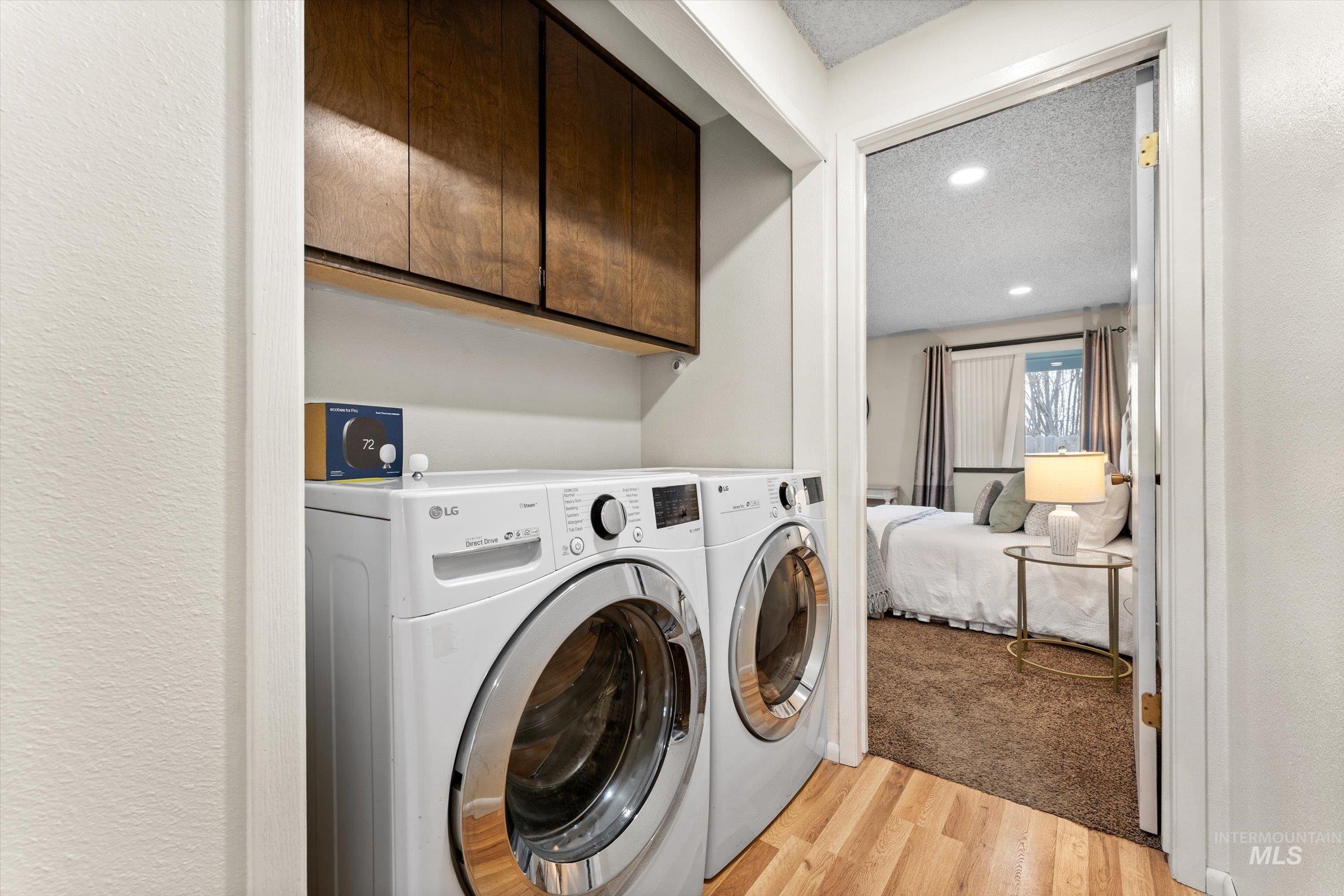 Laundry room featuring a textured ceiling, light wood-type flooring, washer and dryer, cabinet space, and recessed lighting