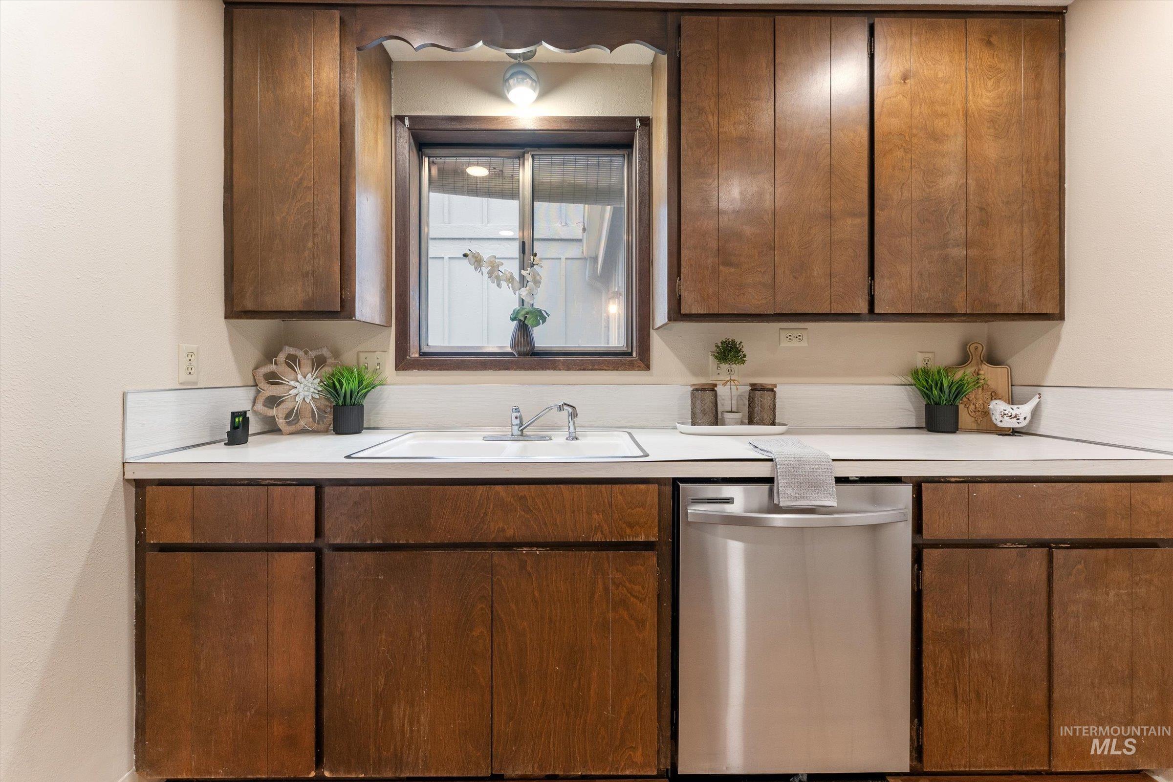 Kitchen featuring dishwasher, light countertops, and dark wood finish cabinets