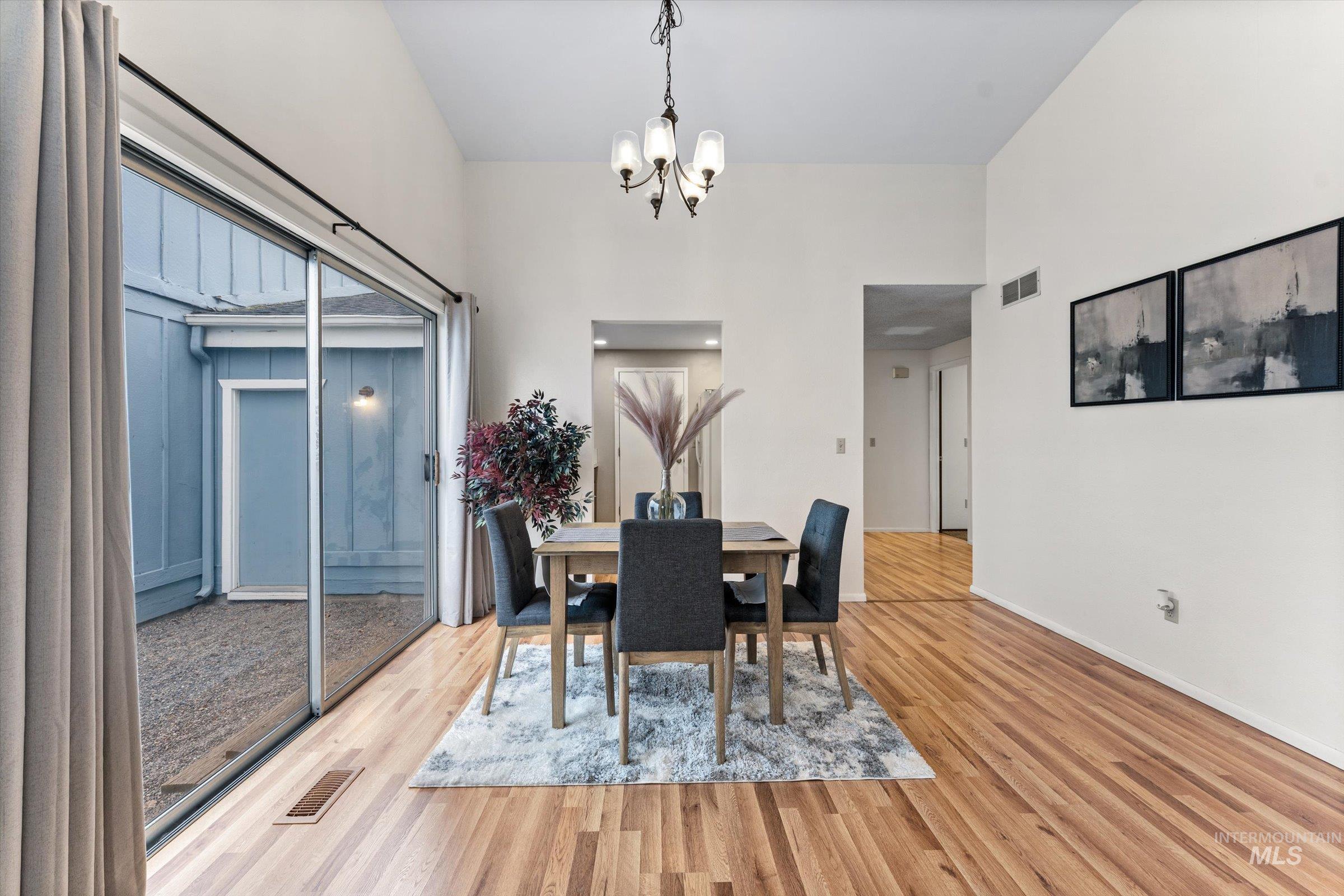 Dining space with suspended lighting, light wood finished floors, and a high ceiling