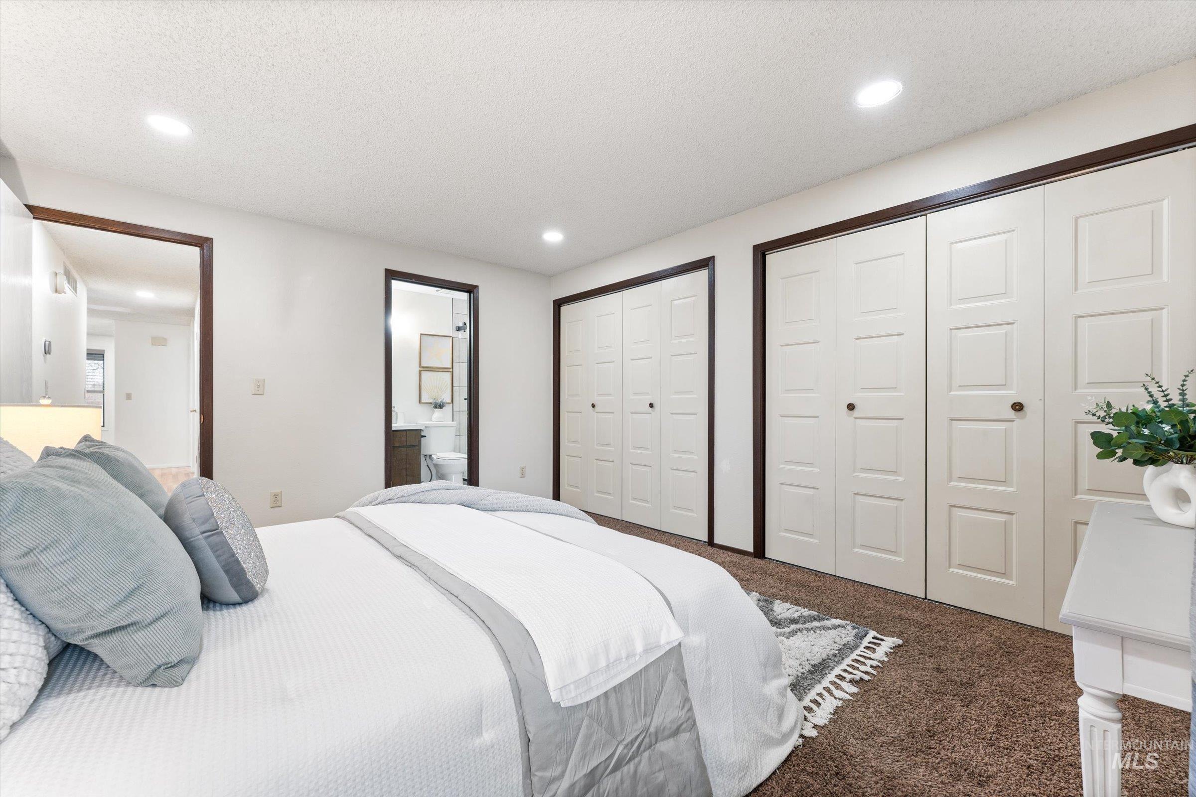 Bedroom featuring two closets, dark colored carpet, a textured ceiling, and recessed lighting