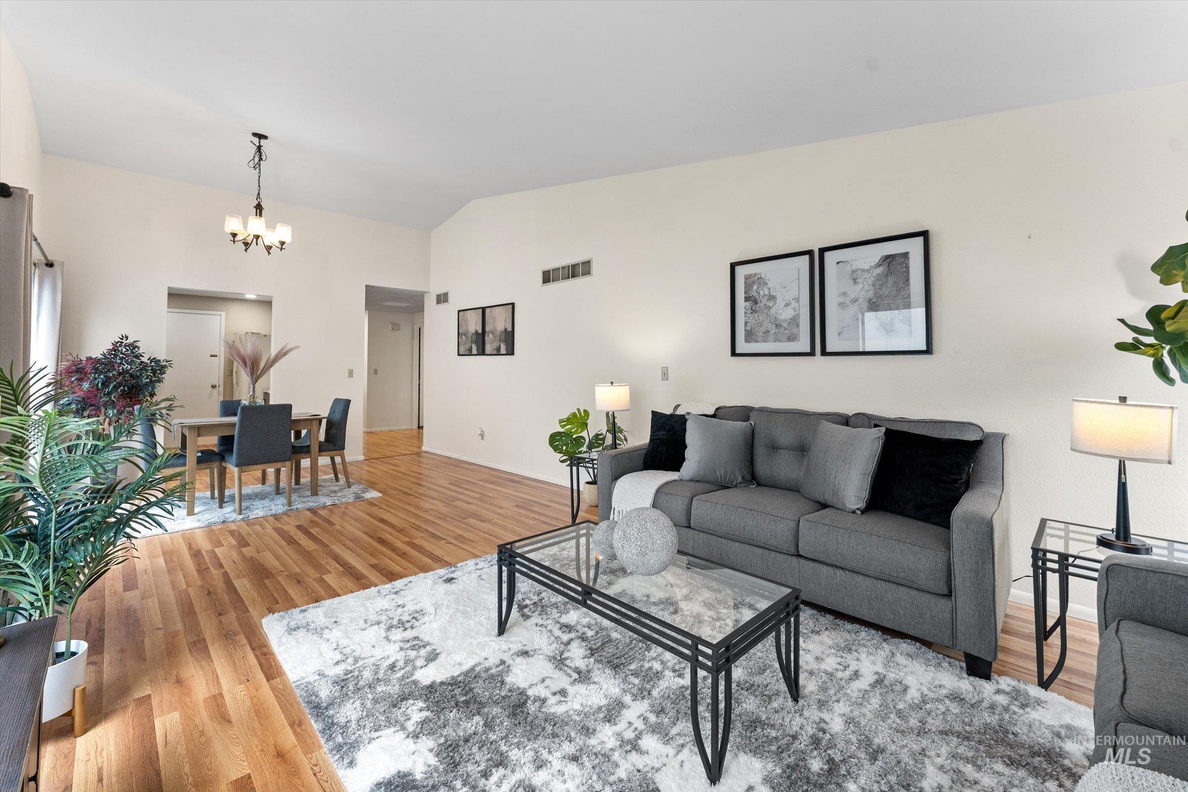 Living room with light wood-style flooring, suspended lighting, and vaulted ceiling