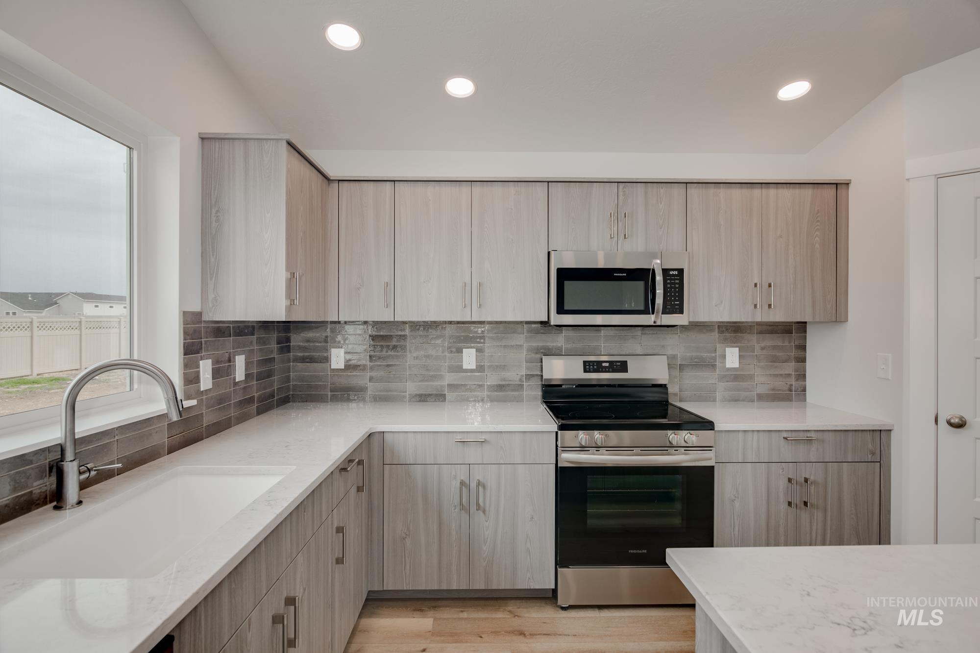 Modern kitchen featuring wood-finish cabinetry, stainless steel appliances, a tile backsplash, light-toned countertops, and recessed lighting