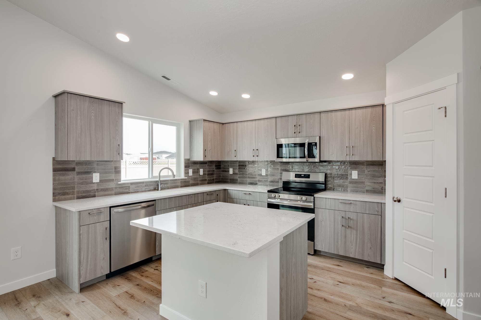 Contemporary kitchen featuring light wood-finish cabinetry, stainless steel appliances, a center island with a white countertop, and a tiled backsplash