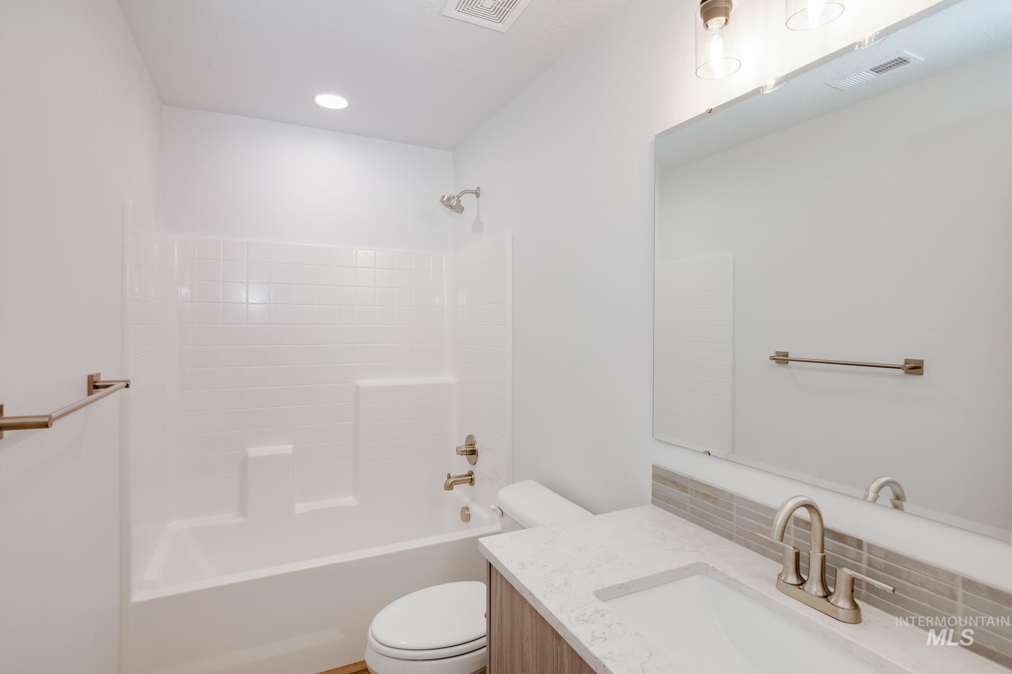 Bathroom featuring a tub/shower combination with white subway tile surround, a single vanity with a white countertop and rectangular sink, and a large wall-mounted mirror