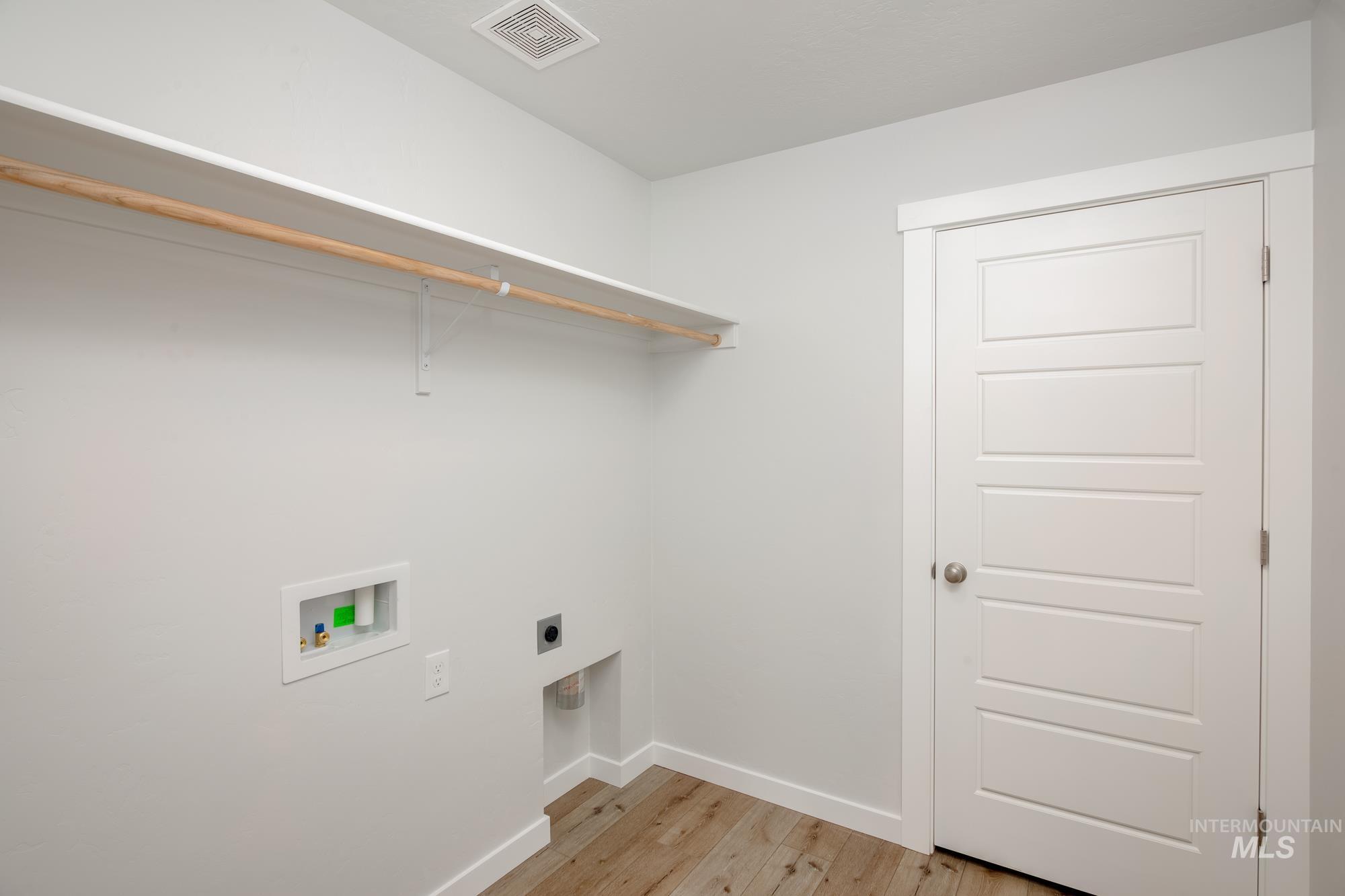 Laundry area featuring wood-finish flooring, white walls, and a multi-panel interior door