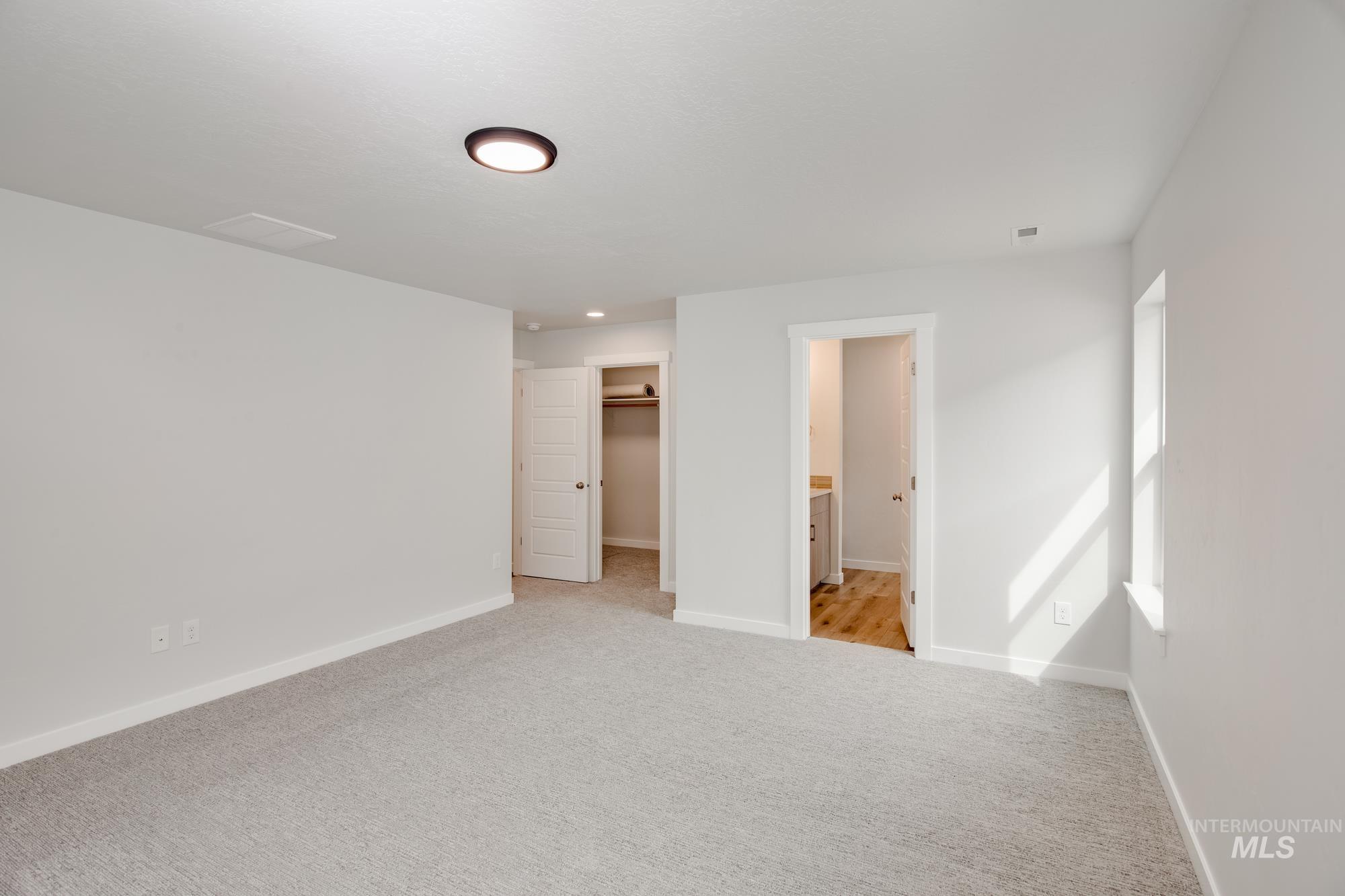 Spacious room featuring light gray carpeting, white walls, and a recessed ceiling light