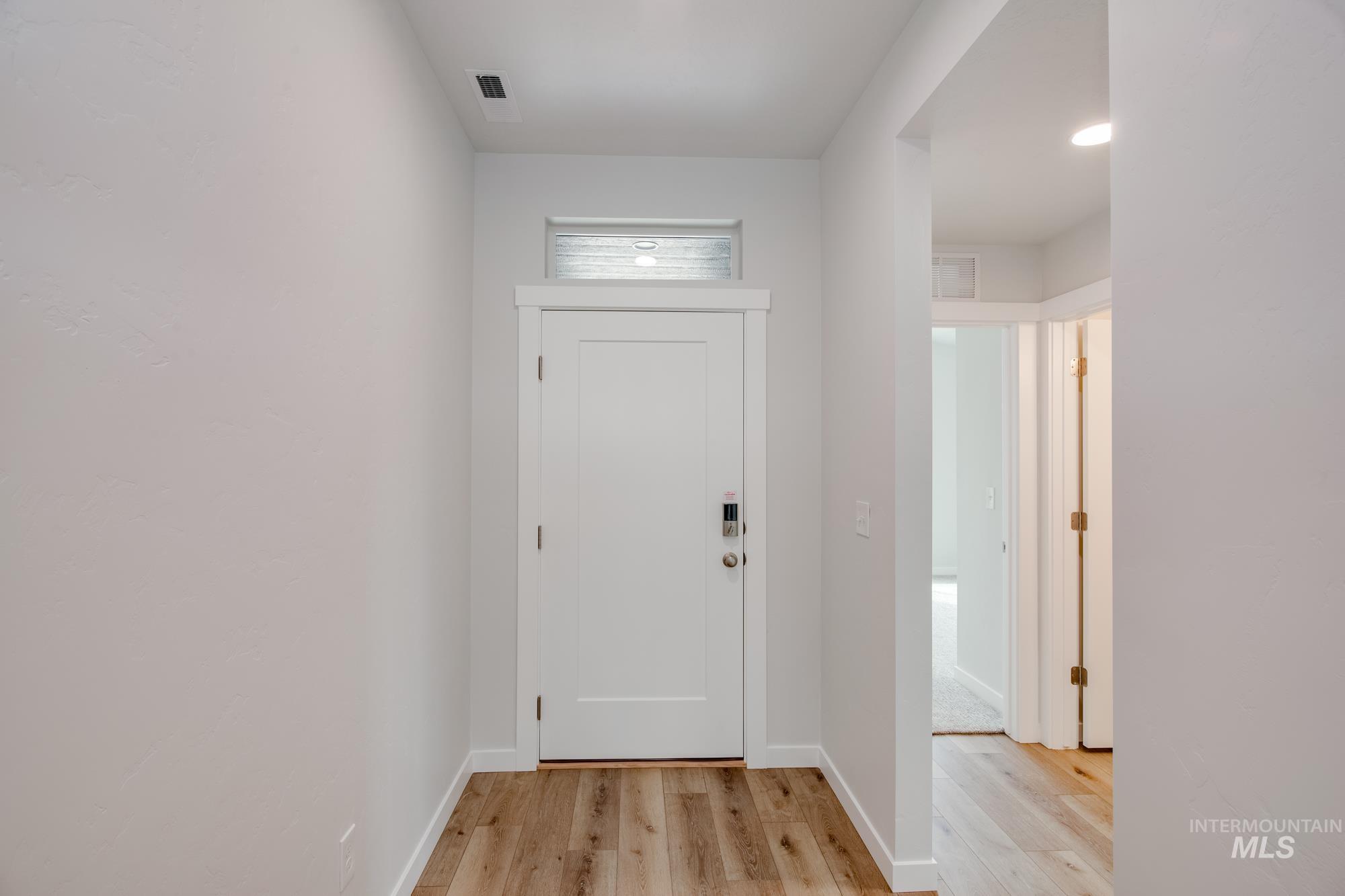 Entryway featuring wood-finish flooring, a contemporary white door with a transom window, and white baseboards