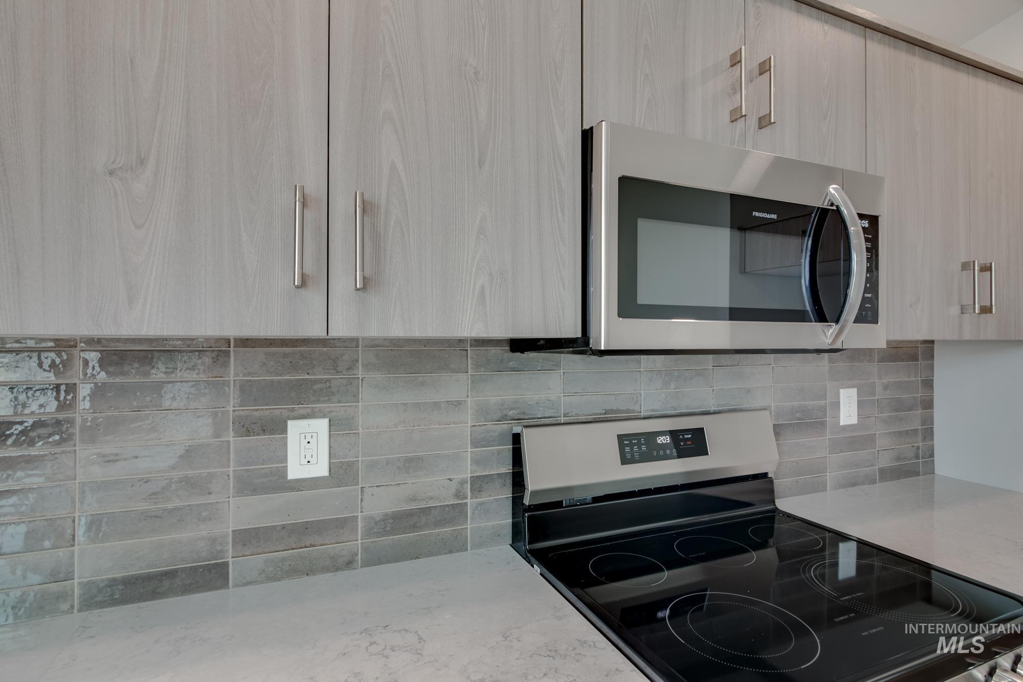 Modern kitchen featuring gray wood-finish cabinetry, stainless steel appliances, and a sleek glass cooktop