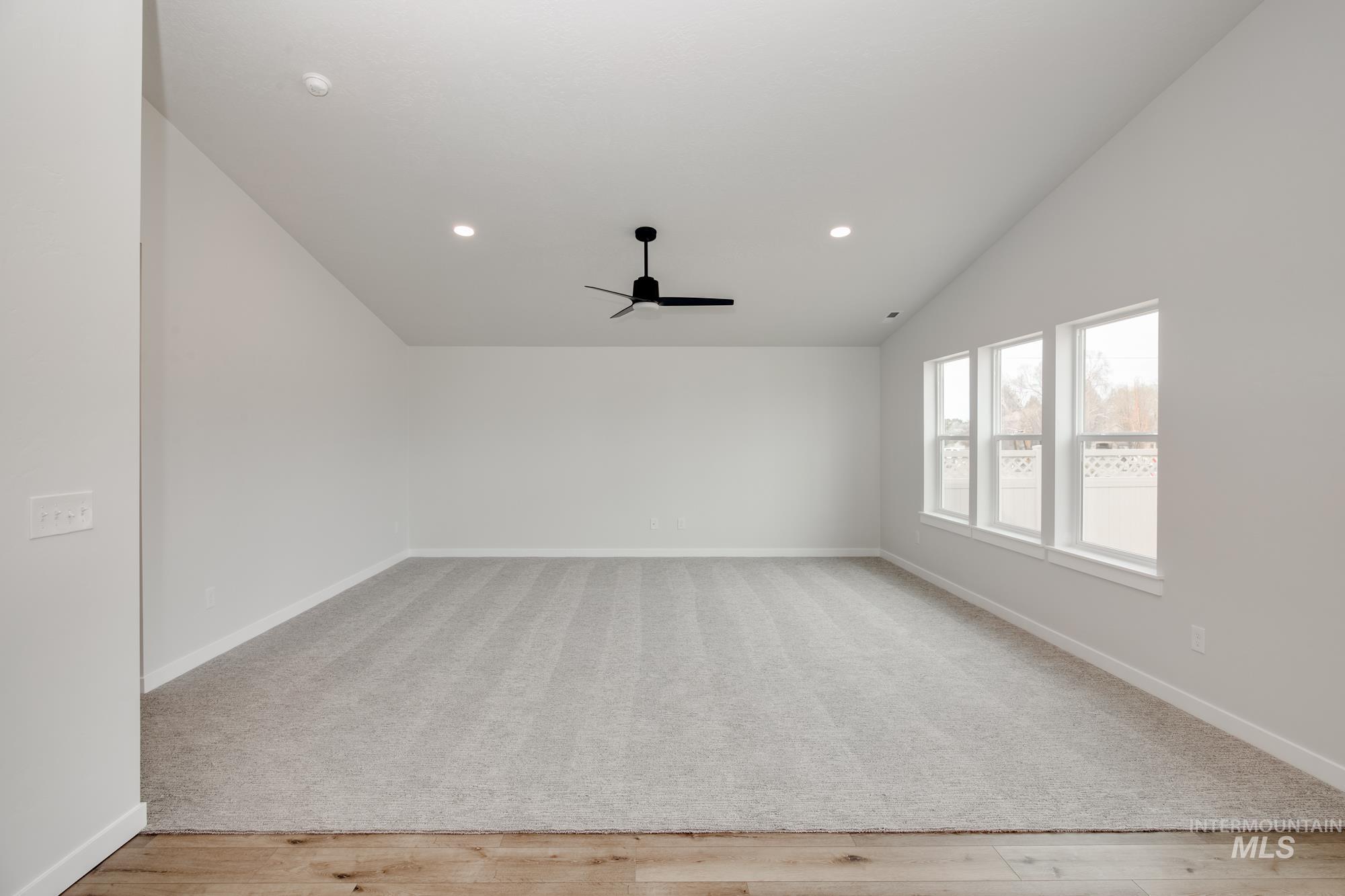 Spacious room featuring vaulted ceilings, recessed lighting, a modern black ceiling fan, light gray carpeting, and a series of three large windows