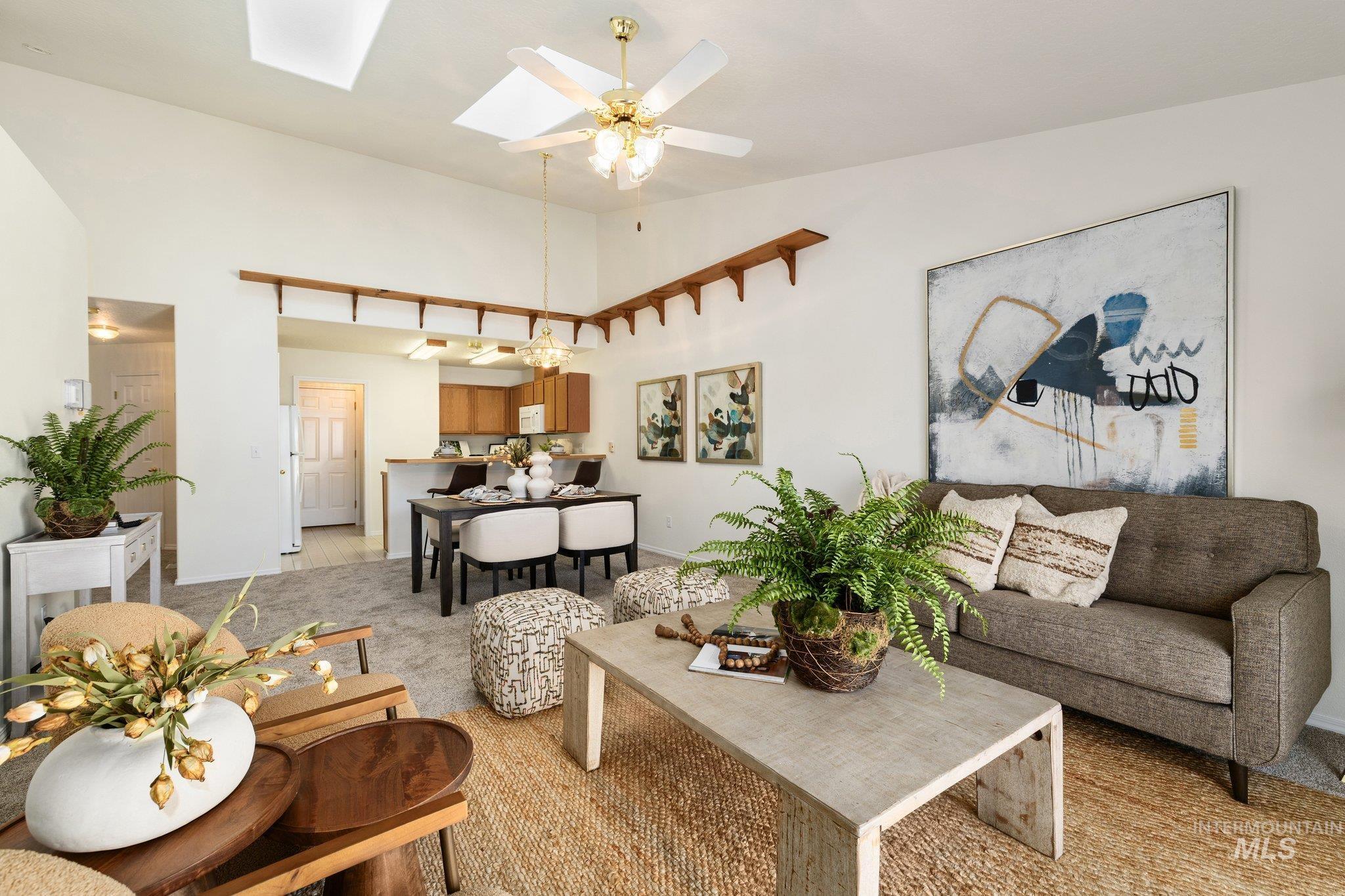 Living area featuring light carpet, a skylight, a towering ceiling, and a ceiling fan