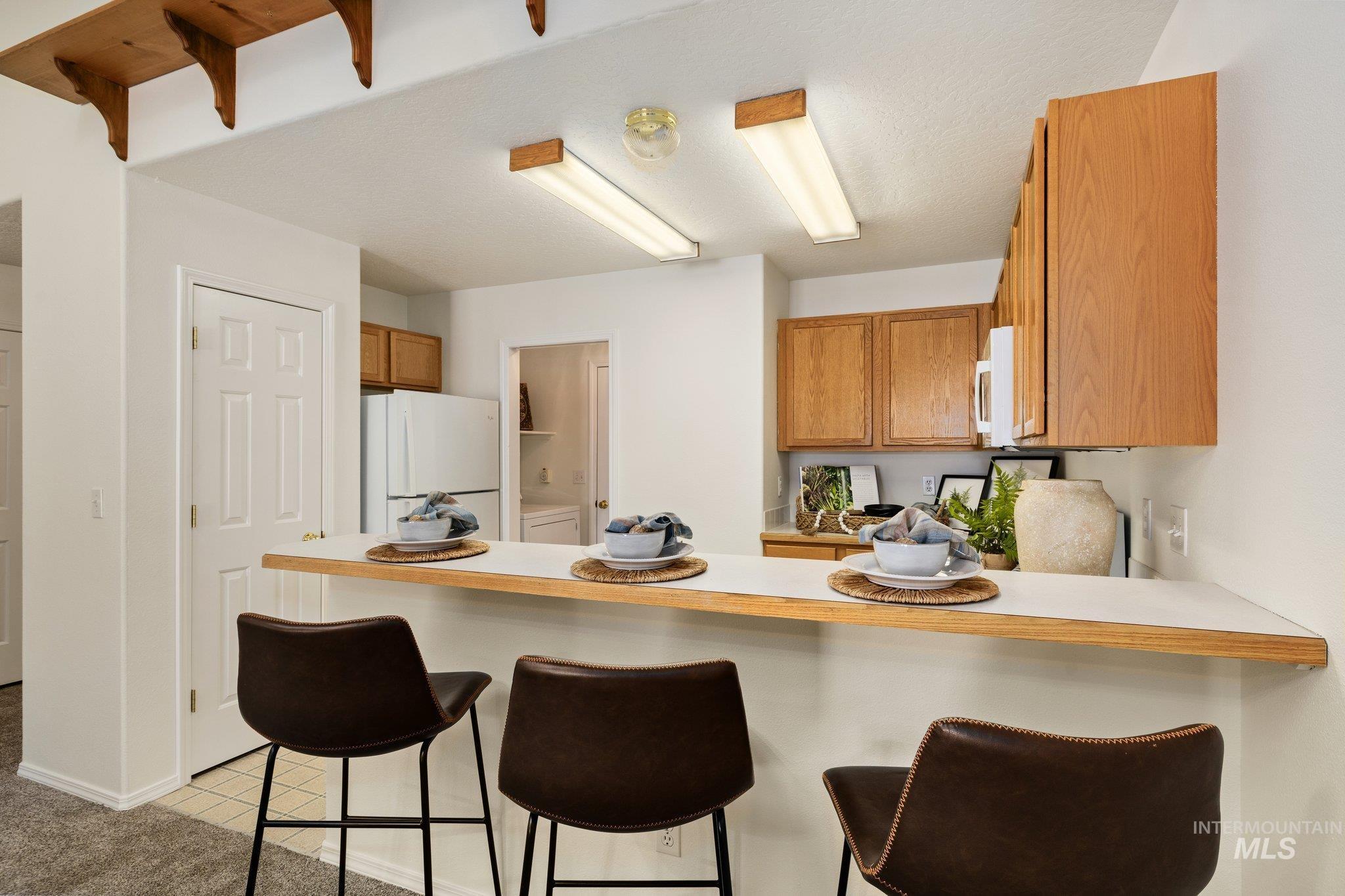 Kitchen featuring a kitchen bar, light countertops, white appliances, brown cabinets, and a peninsula