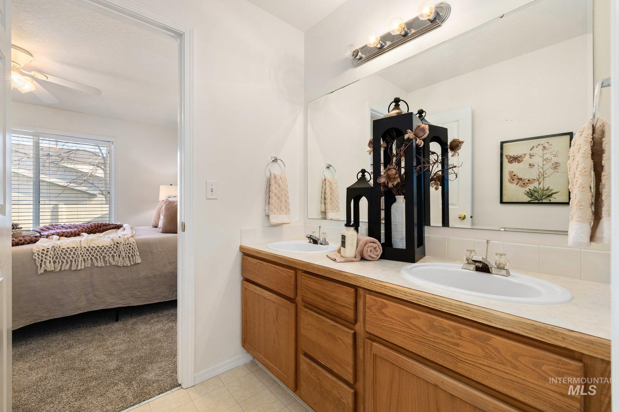 Ensuite bathroom with double vanity, light colored carpet, a ceiling fan, and light tile patterned floors