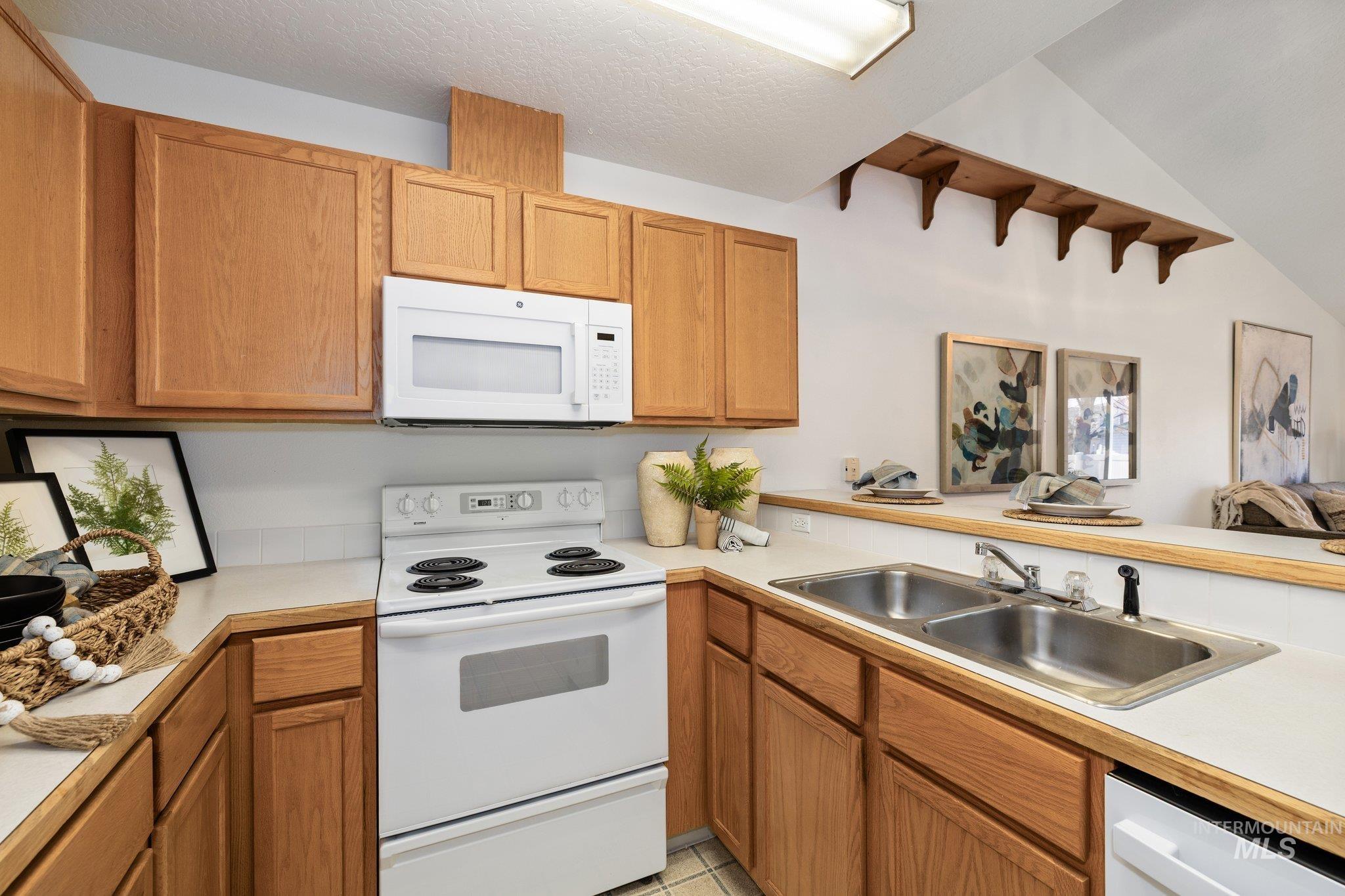 Kitchen with white appliances, light countertops, brown cabinetry, and vaulted ceiling