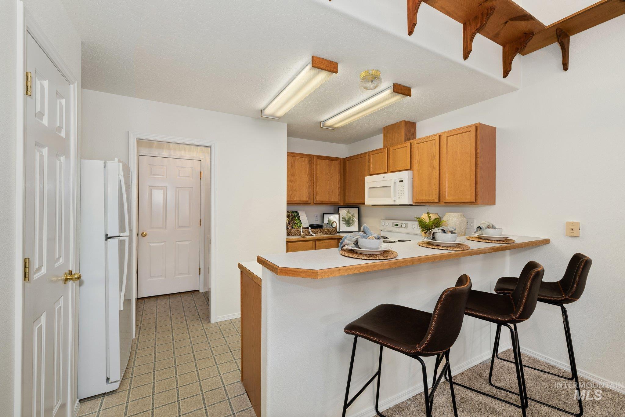 Kitchen with a kitchen breakfast bar, white appliances, light countertops, a peninsula, and brown cabinetry