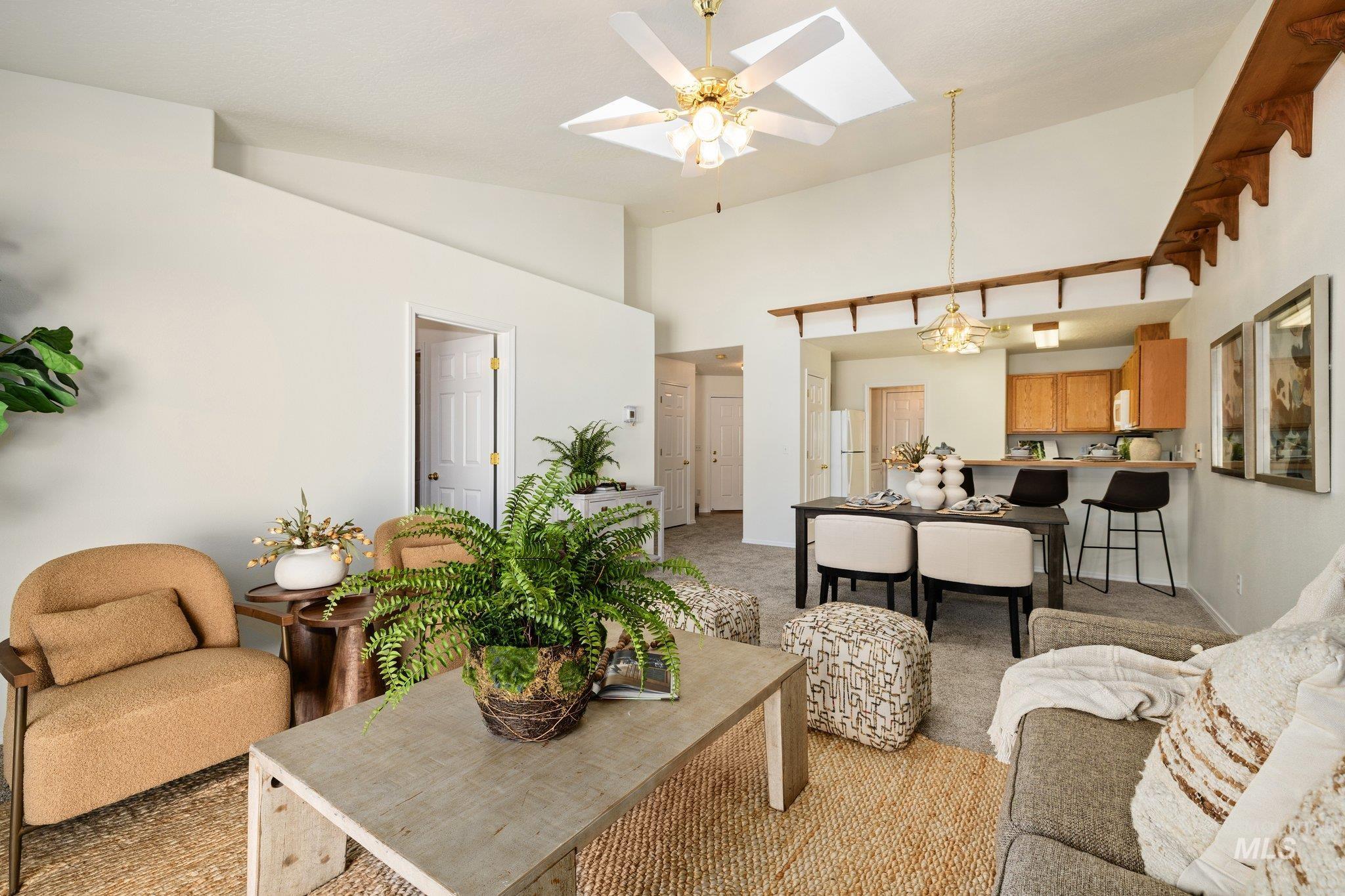 Living area with a skylight, light carpet, high vaulted ceiling, ceiling fan, and a chandelier