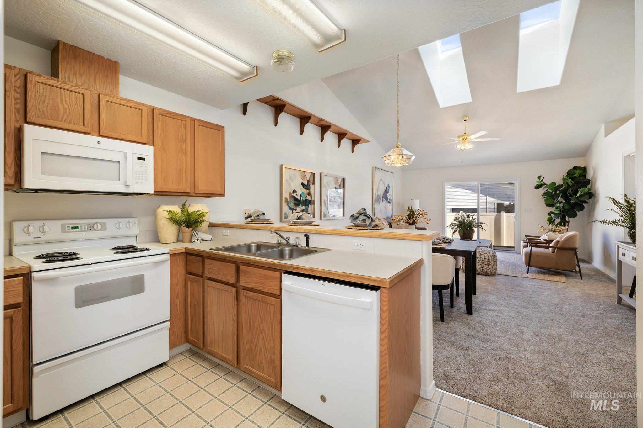 Kitchen featuring white appliances, a skylight, hanging light fixtures, vaulted ceiling, and a peninsula