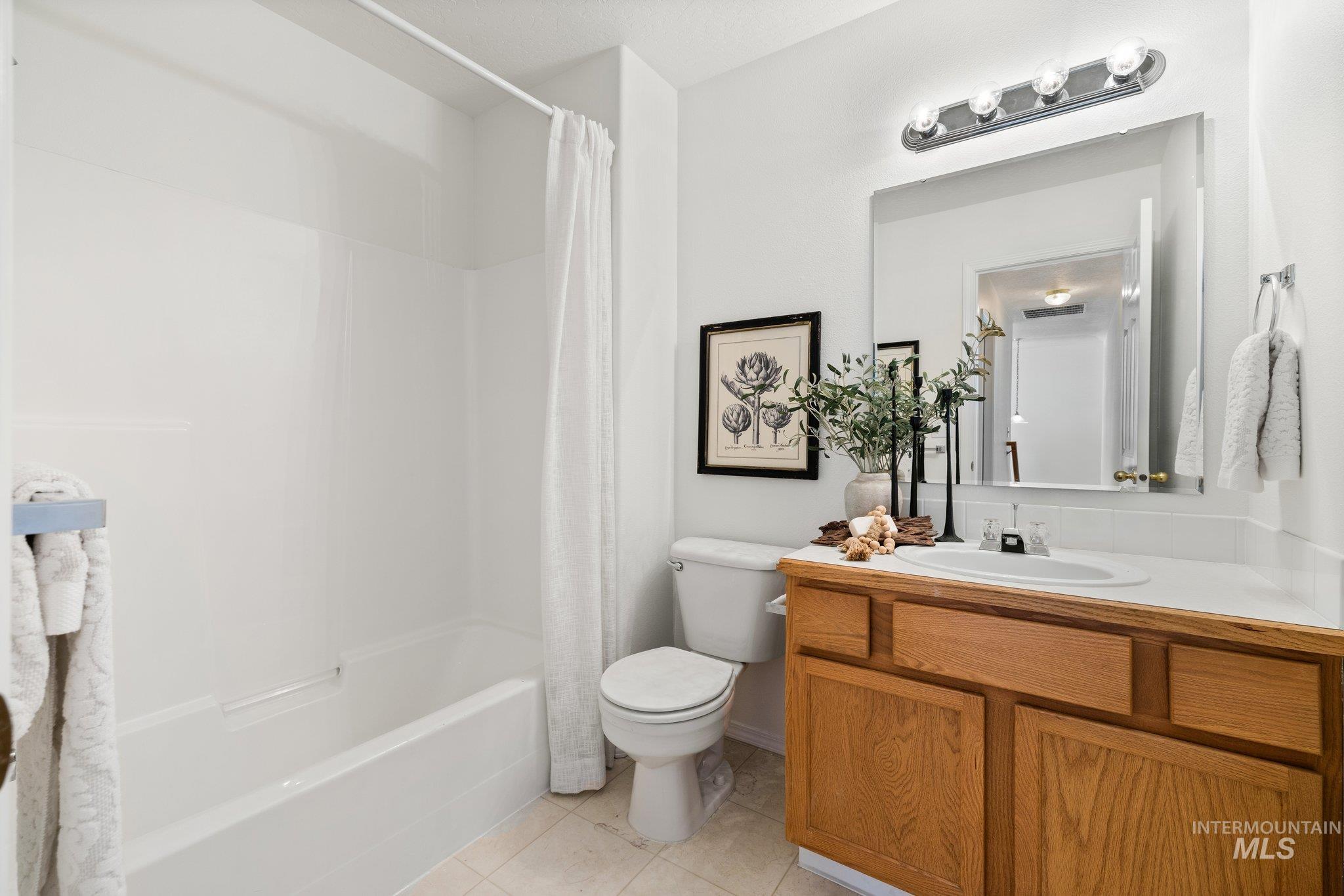 Full bath featuring vanity, shower / bathtub combination with curtain, and light tile patterned floors