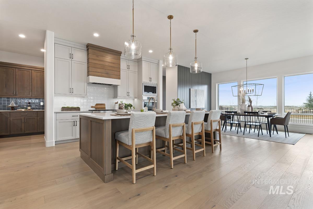 Kitchen featuring a center island with sink, light wood finished floors, pendant lighting, white cabinetry, and backsplash