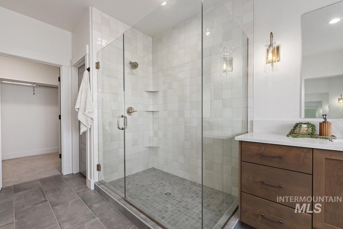 Bathroom featuring vanity, a walk in closet, a stall shower, tile patterned flooring, and recessed lighting
