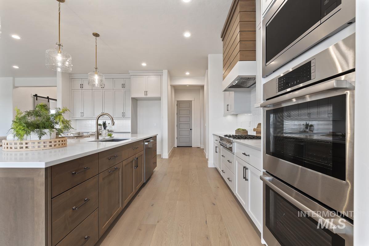 Kitchen with appliances with stainless steel finishes, white cabinetry, pendant lighting, light wood-style flooring, and recessed lighting