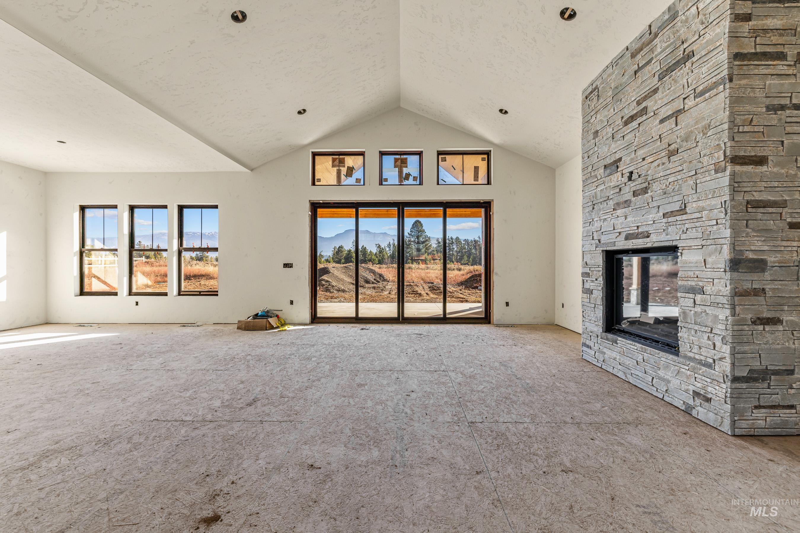 Unfurnished living room with a mountain view, a stone fireplace, high vaulted ceiling, a textured ceiling, and carpet floors