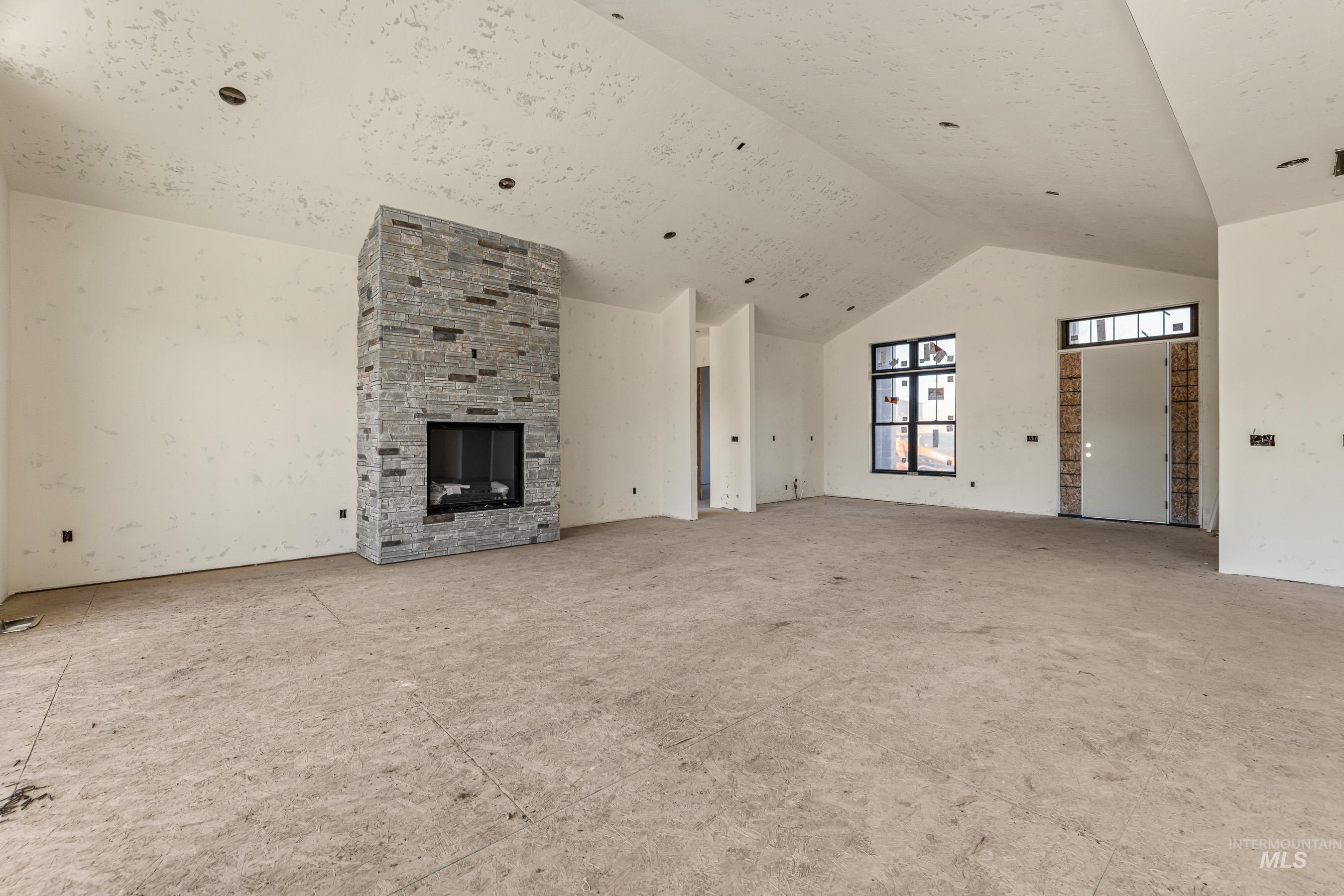 Unfurnished living room with high vaulted ceiling and a stone fireplace
