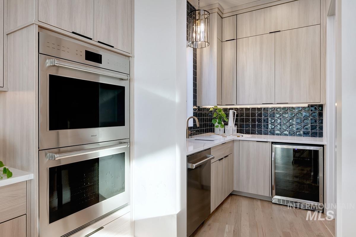 Kitchen featuring stainless steel appliances, light brown cabinets, pendant lighting, wine cooler, and light stone counters